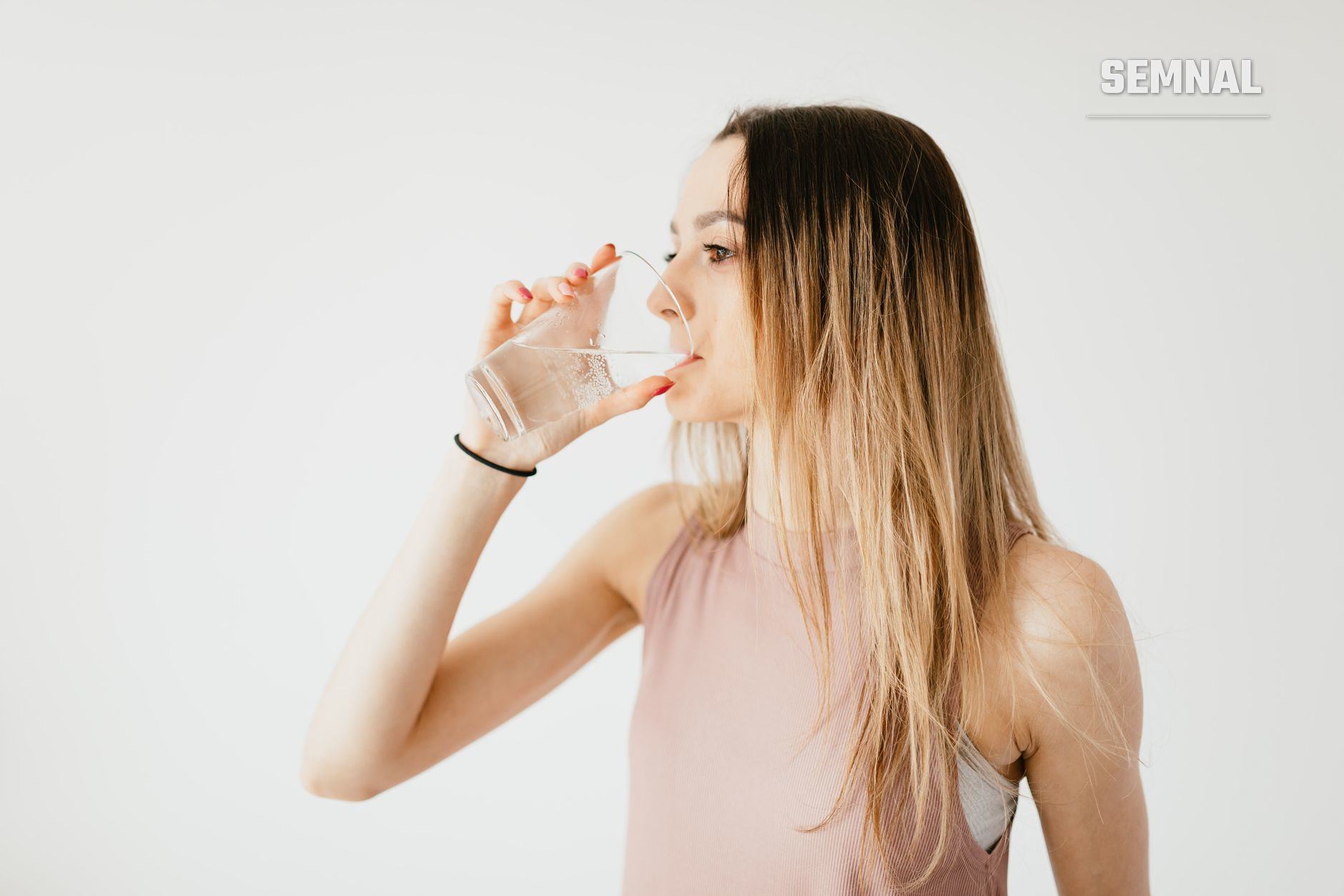 Femeie care bea apa dintr-un pahar transparent, ilustrand hidratarea corecta a corpului adult