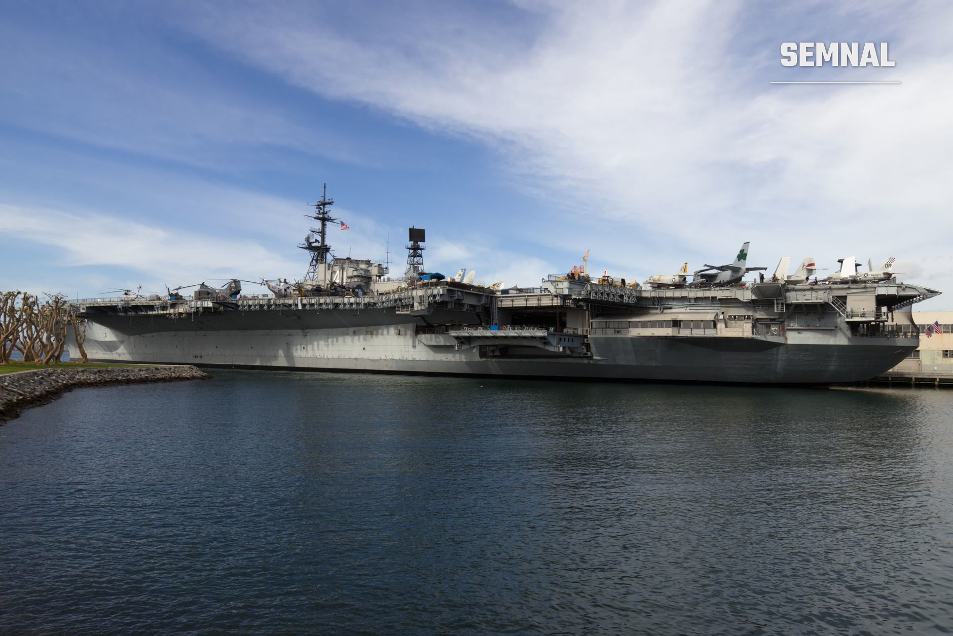Portavionul USS George Washington ancorат în port, văzut din lateral, cu suprastructura militară și pista de aterizare bine vizibilă pe puntea superioara a navei.