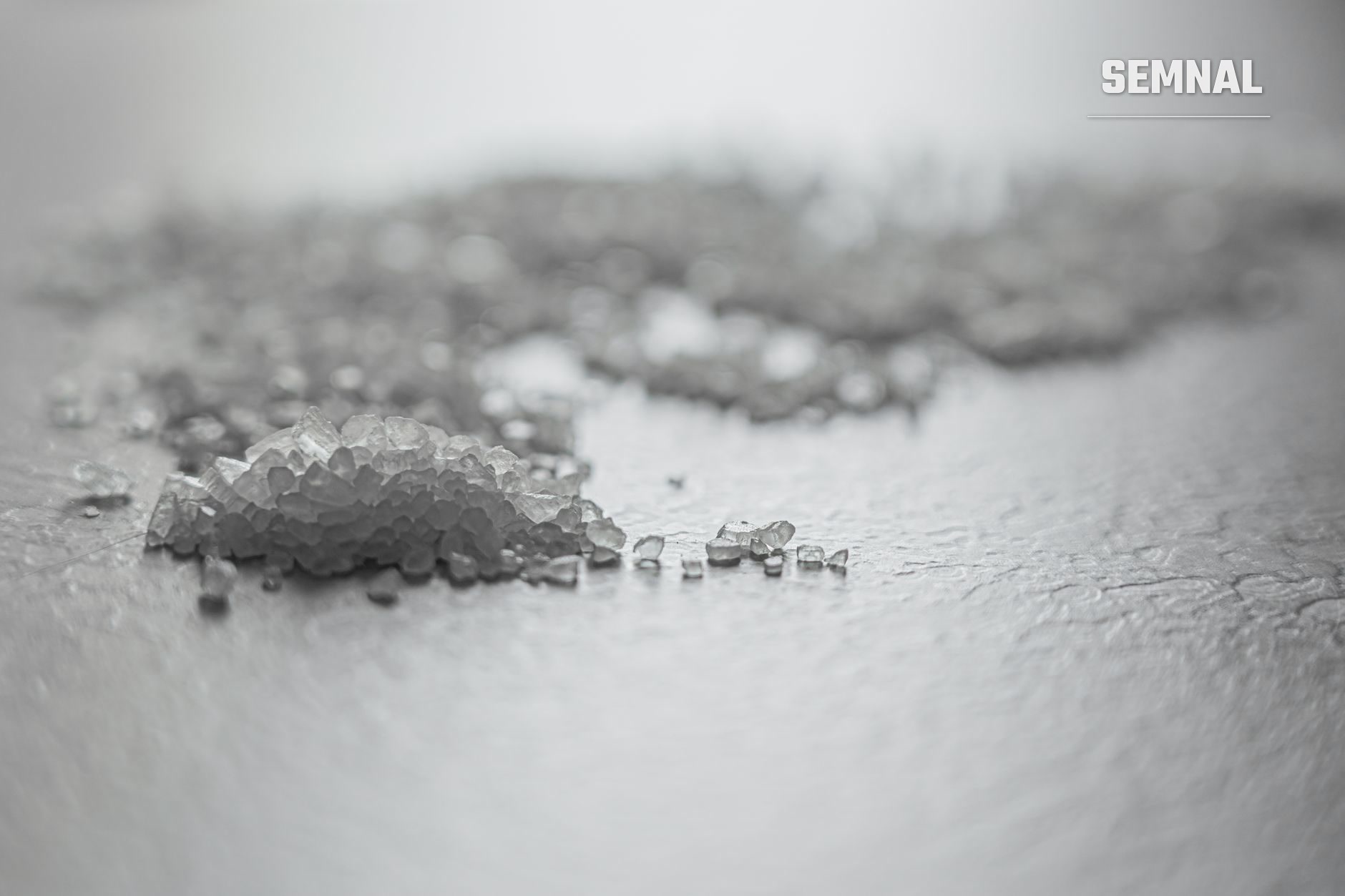 Cristale mari de sare gri-alburie pe suprafață plană, macro fotografie care evidențiază textura și granulația sării de mare în comparație cu cea rafinată.