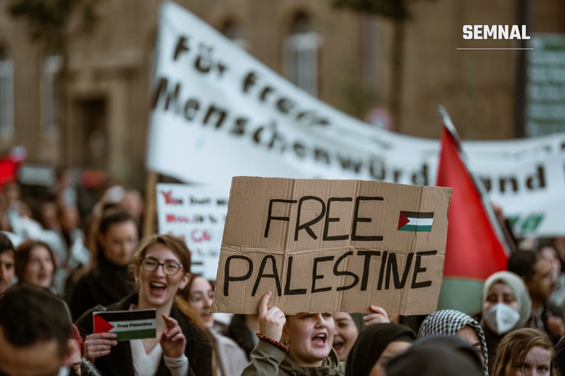 Manifestație de stradă cu activiști ținând semn din carton scris 'FREE PALESTINE' și steag palestinian, în sprijinul cauzei palestiniene.