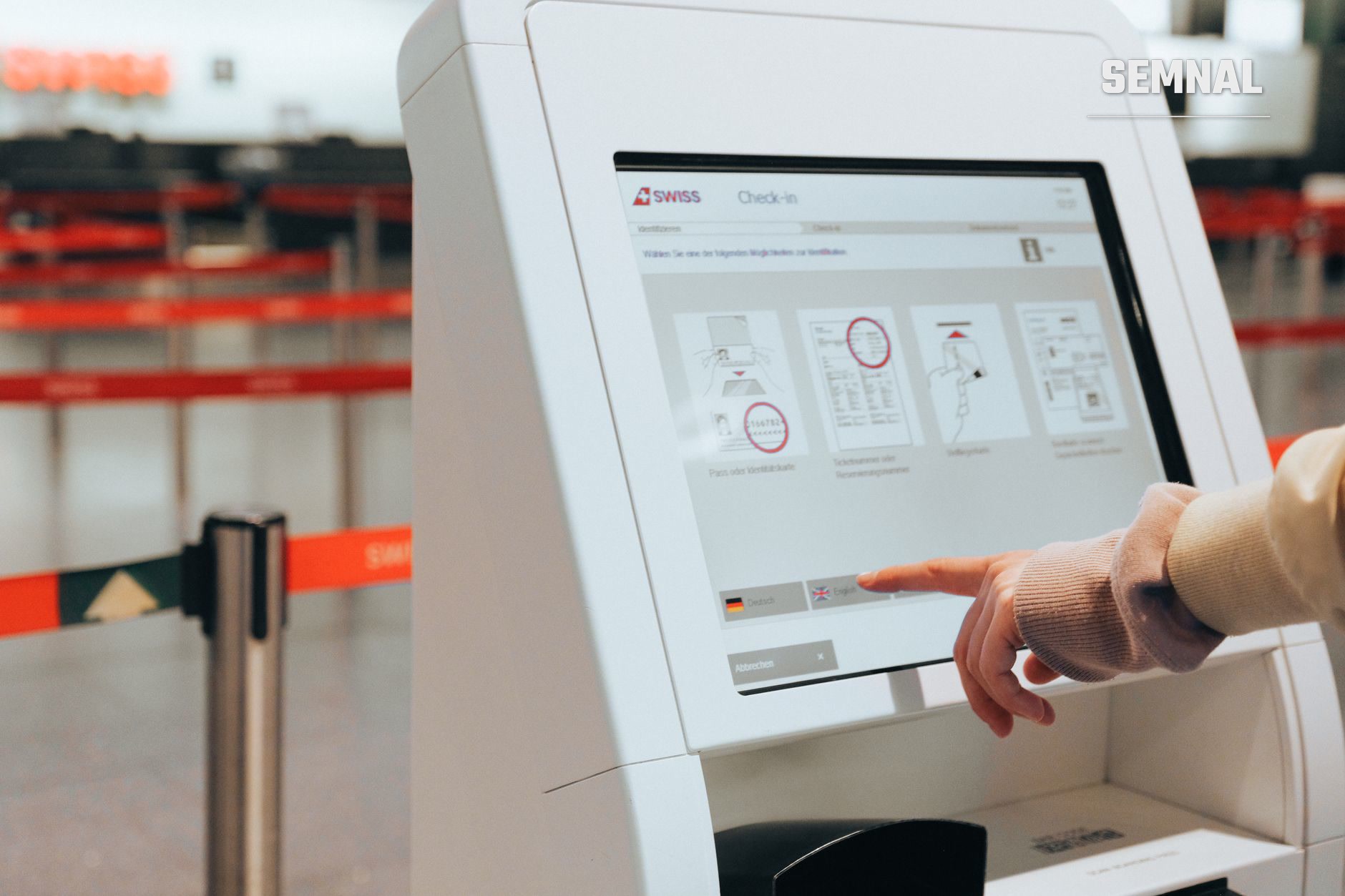 Pasager folosind terminalul de check-in SWISS cu ecran tactil pentru a-și alege locul la avion, cu cozi de așteptare vizibile în fundal