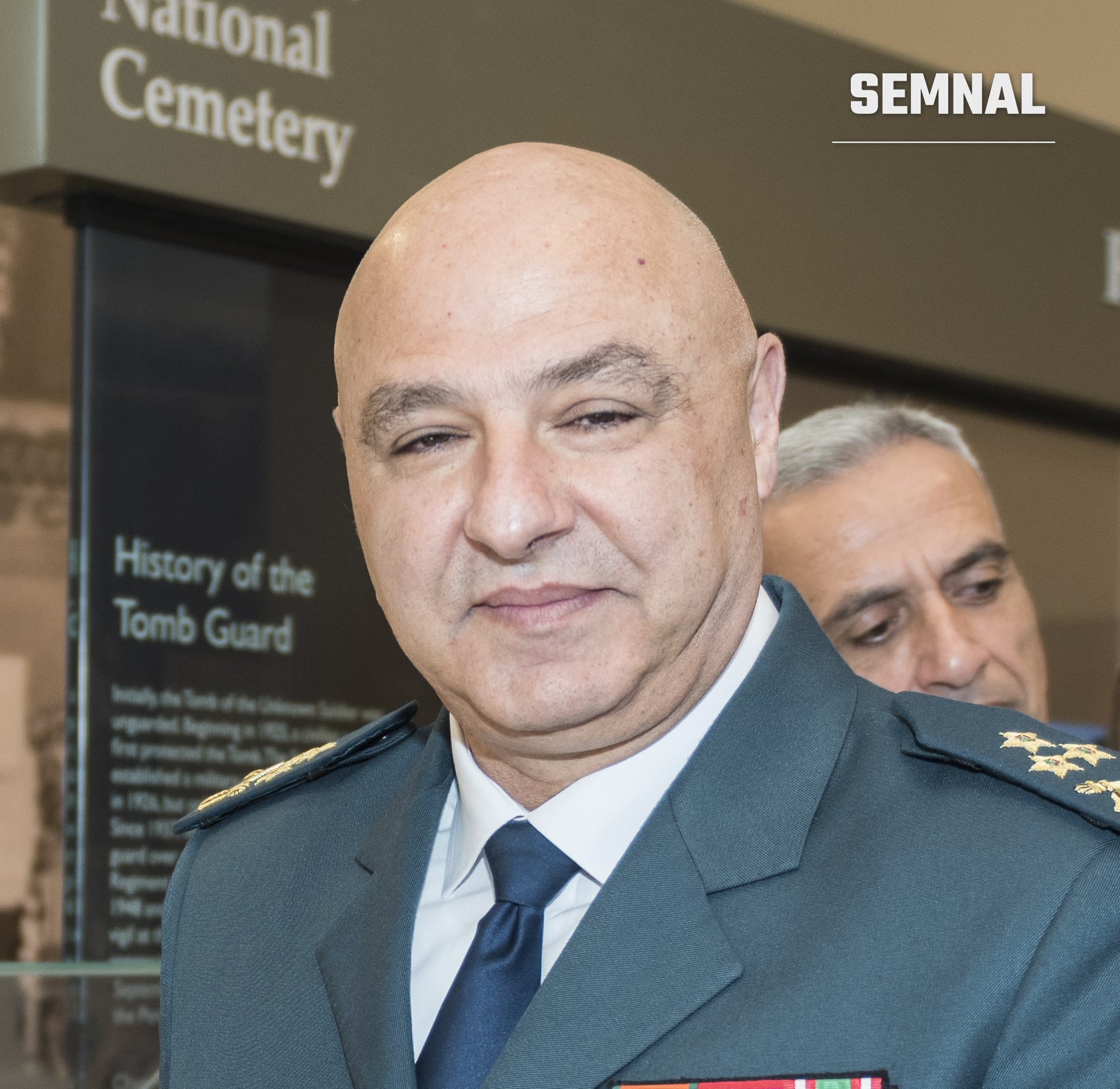 Joseph Aoun, președintele Libanului, purtând uniformă militară gri cu decorații și eșarfă albastră, fotografiat la o instituție oficială cu panou informativ în fundal. (Foto: Arlington National Cemetery)