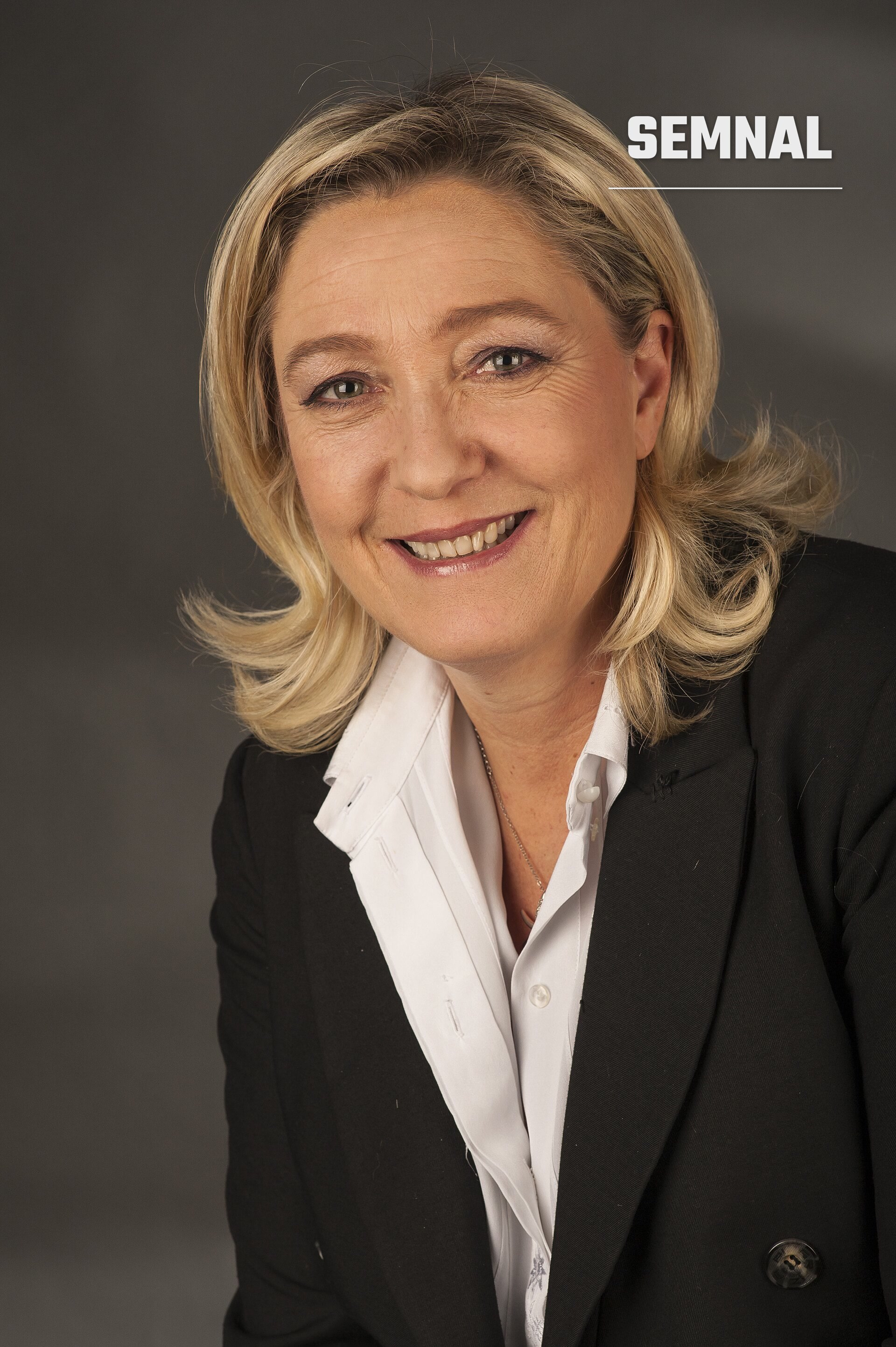Marine Le Pen, portret oficial în costum negru și cămașă albă, zâmbând la cameră pe fond gri neutru. (Foto: Foto-AG Gymnasium Melle)