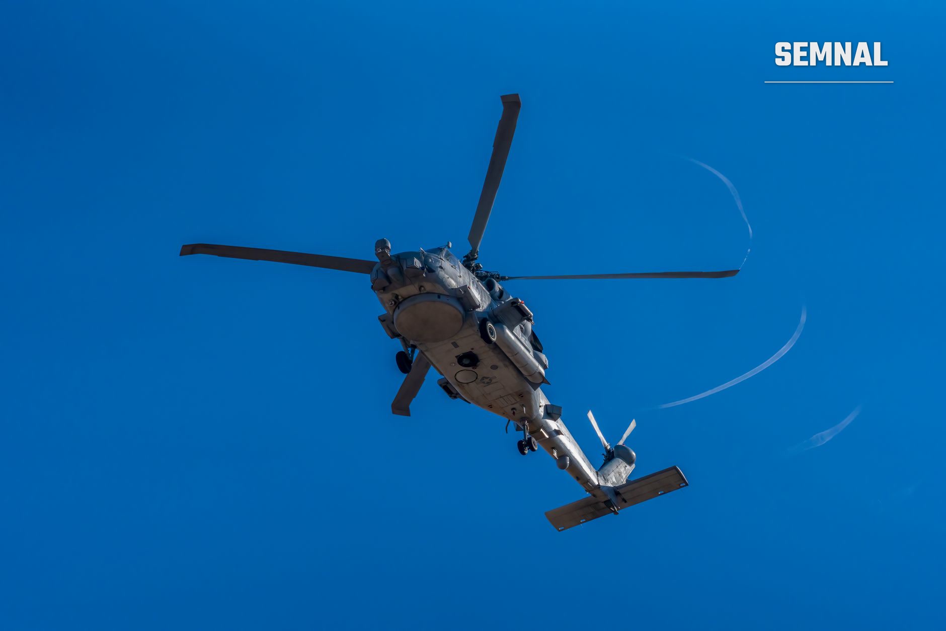 Elicopter militar gri-alb în zbor pe cer albastru, fotografiat din jos, cu patru pale rotative și fuselaj detaliat vizibil. (Foto: Rafael Minguet Delgado / Pexels)