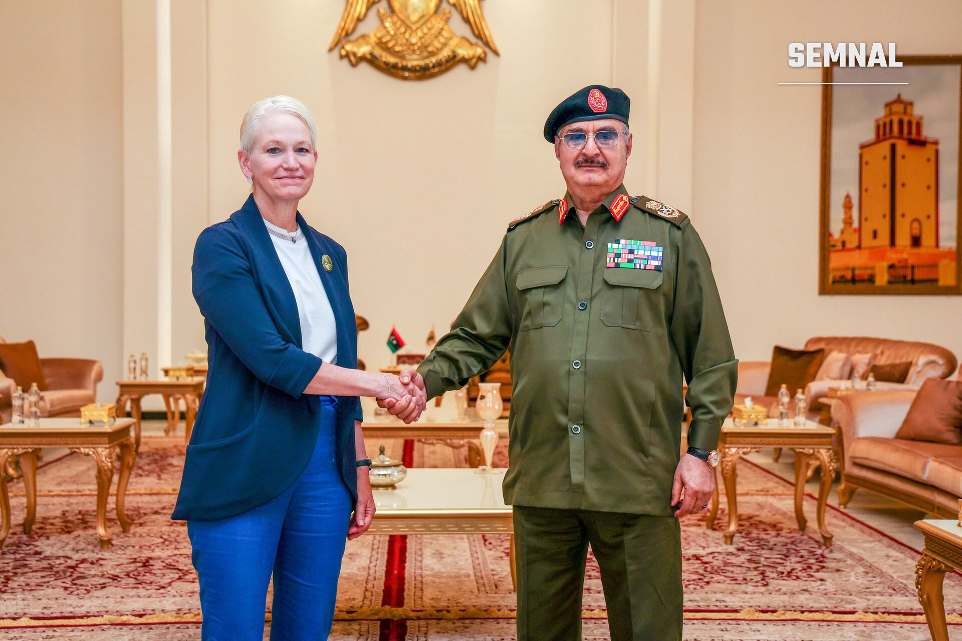 Khalifa Haftar, comandant, strângând mâna unei femei într-o sală oficial decorate, purtând uniformă militară și baretă neagră. (Foto: US Government)
