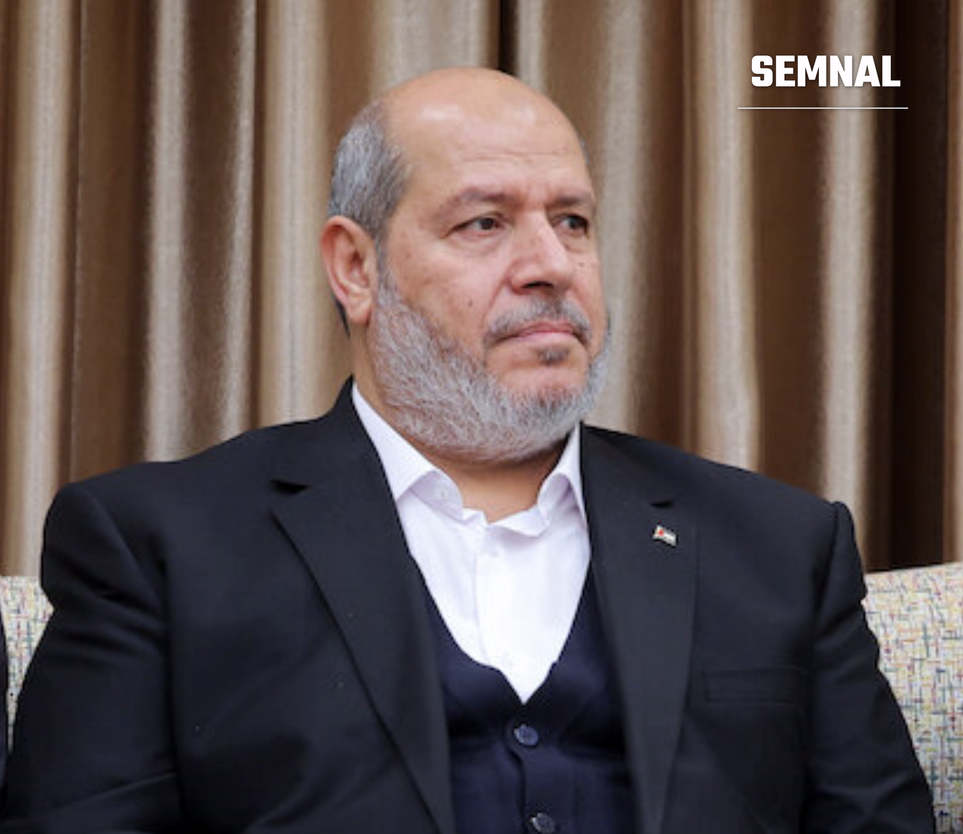 Khalil al-Hayya, lider Hamas, portret în plan apropiat, îmbrăcat formal cu costum negru și cămașă albă, ședință într-un interior elegant cu draperii, expresie serioasă. (Foto: Khamenei.ir)