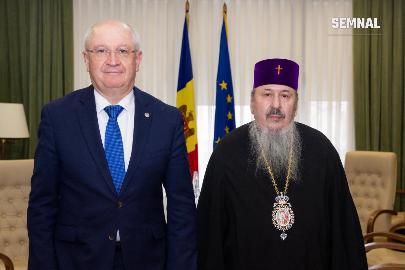 Alexandru Munteanu, vicepreședinte USR, în costum bleumarin și cravată albastră, fotografiat alături de un prelat ortodox cu barbă lungă, în interior formal cu steaguri în fundal. (Foto: Guvernul Republicii Moldova)