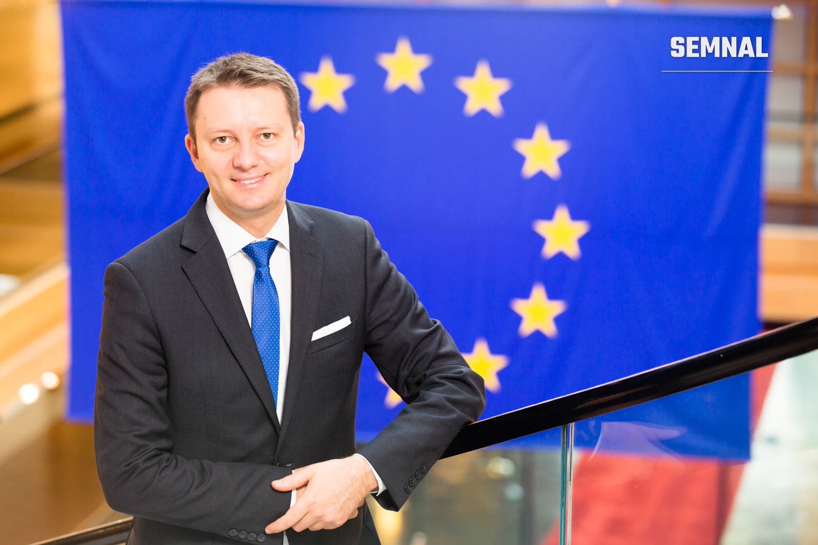Siegfried Mureșan, negociator-șef din partea Parlamentului European, într-o fotografie de presă oficială în costum și cravată, în fața unui steag european. (Foto: AureliaA)
