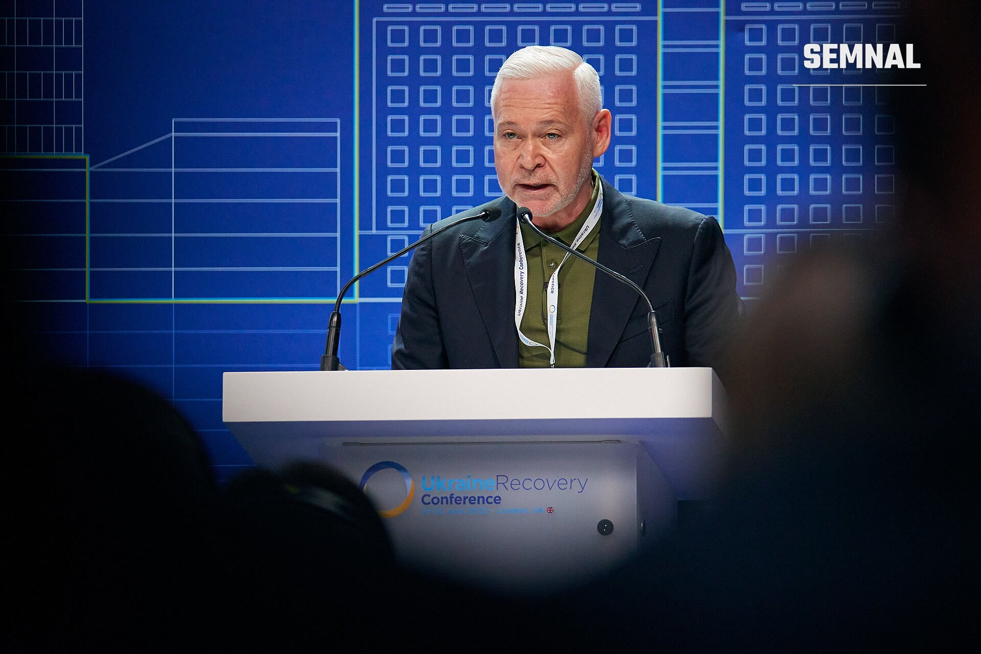 Ihor Terekhov, primar al orașului Harkov, vorbind la pupitrul unei conferințe cu semnul "Ukraine Recovery Conference" pe fundal, purtând un sacou negru și o cămașă verde-oliv. (Foto: Foreign, Commonwealth & Development Office)