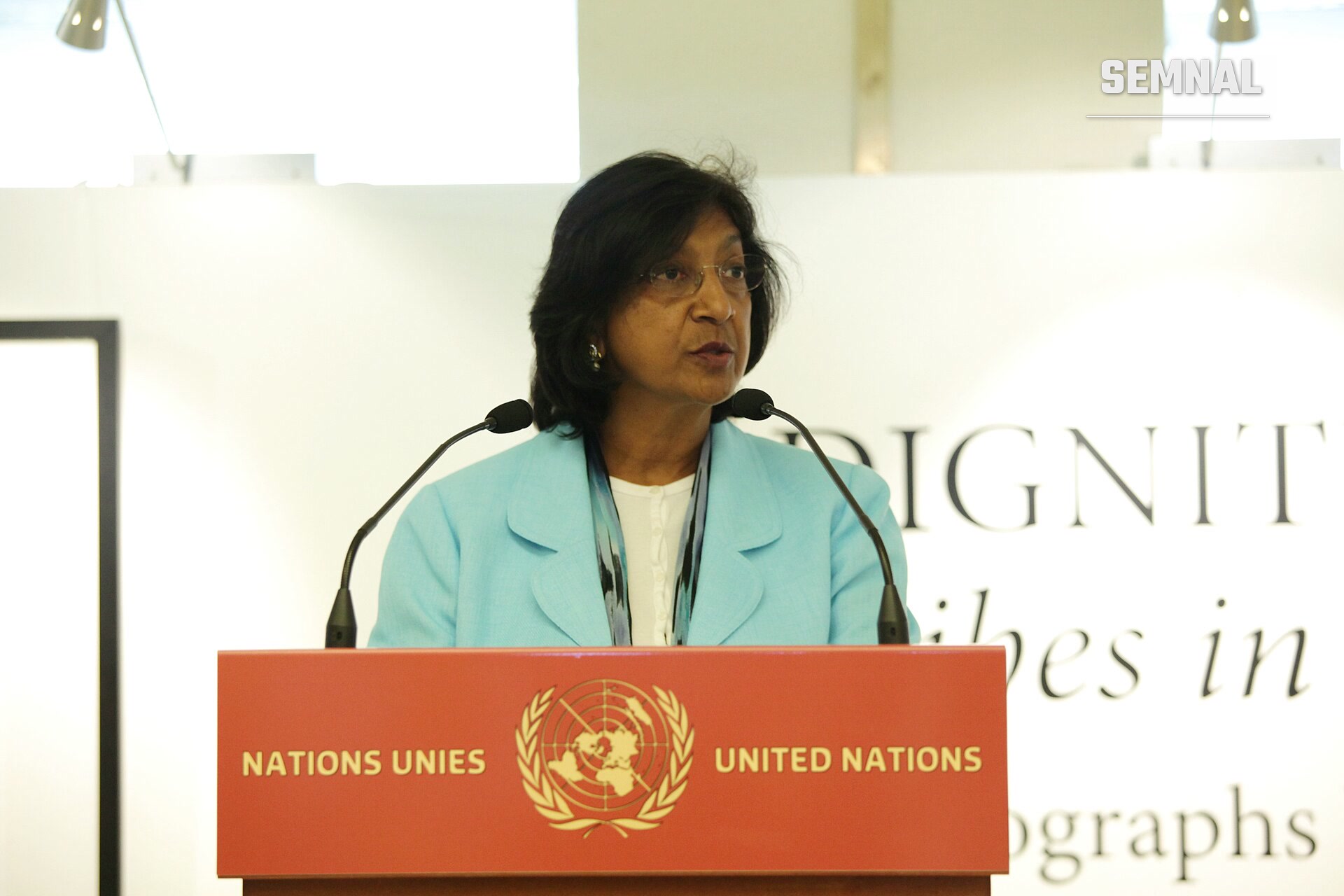 Navanethem "Navi" Pillay, juristă și apărătoare a drepturilor internaționale, vorbind la un podium al Organizației Națiunilor Unite, purtând un sacou albastru deschis și ochelari. (Foto: United States Mission Geneva)