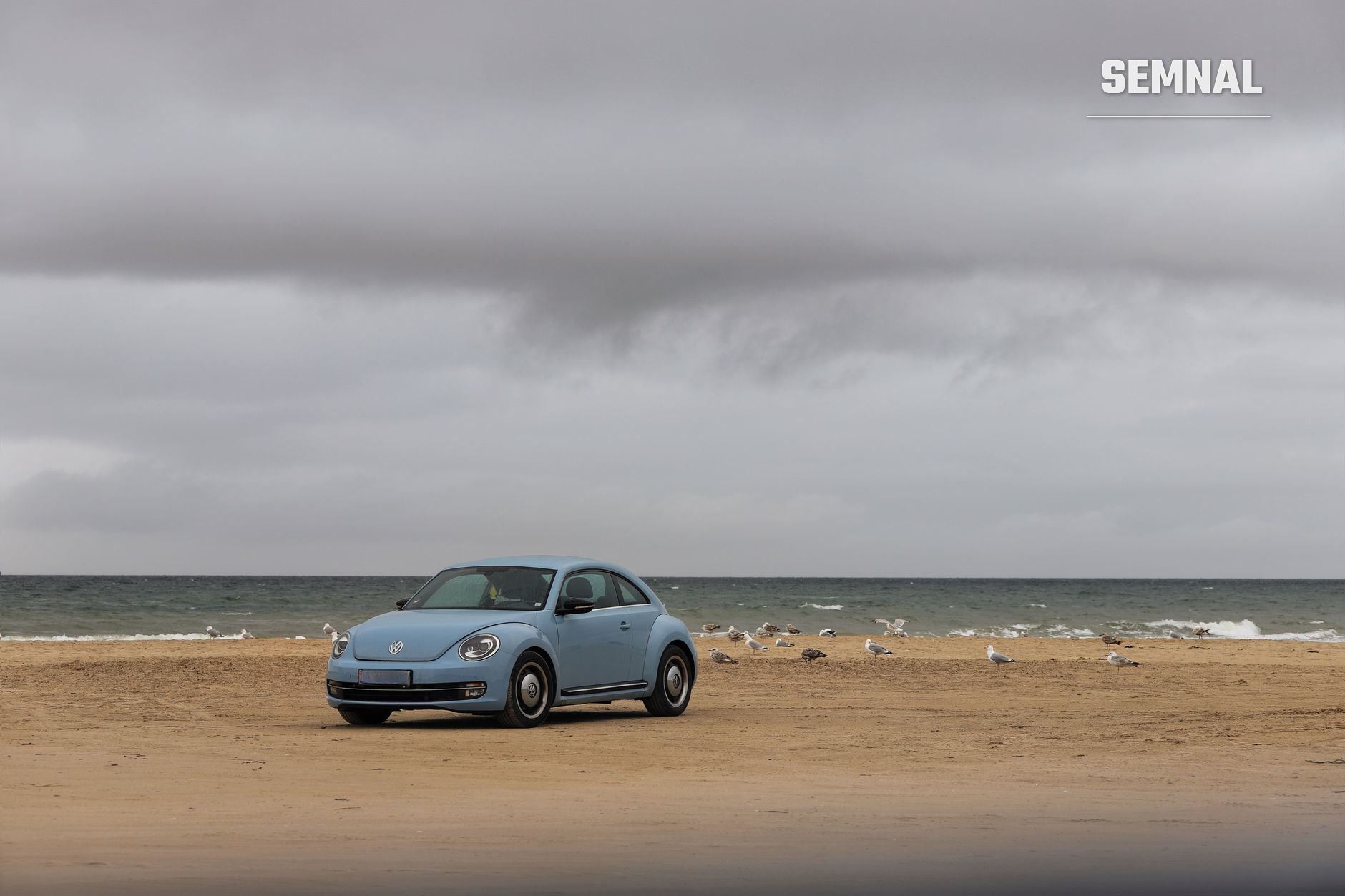 Volkswagen Beetle albastru parcat pe nisipul gol al unei plaje, cu marea agitată și cerul noros în spate, imagine de ilustrație pentru incidentul de la Cap Aurora (Foto: Christina & Peter / Pexels)