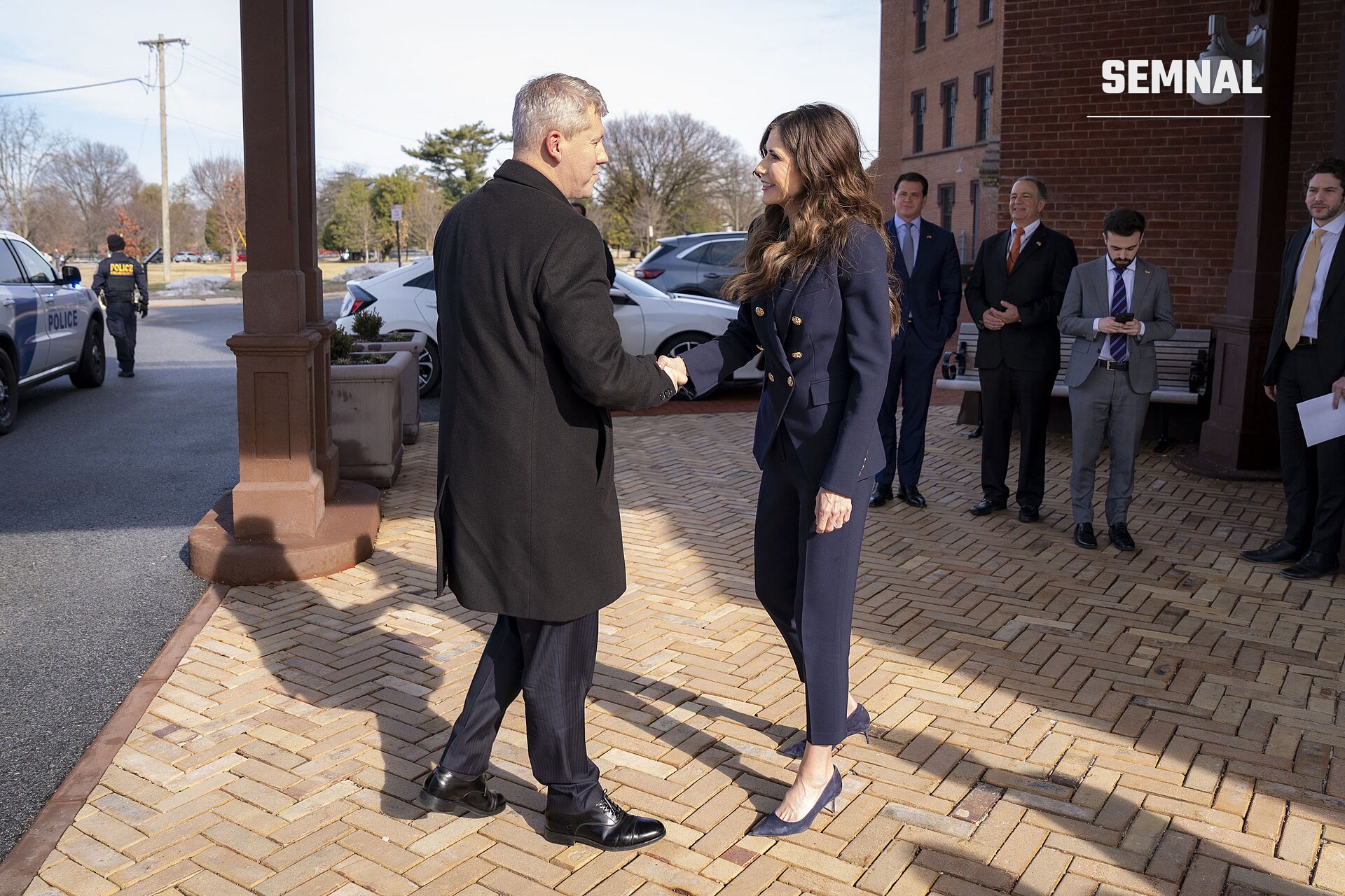 Cătălin Predoiu, ministrul interimar al Afacerilor Interne, salută o persoană în costum bleumarin la un eveniment oficial în fața unei clădiri publice. (Foto: DHSgov)