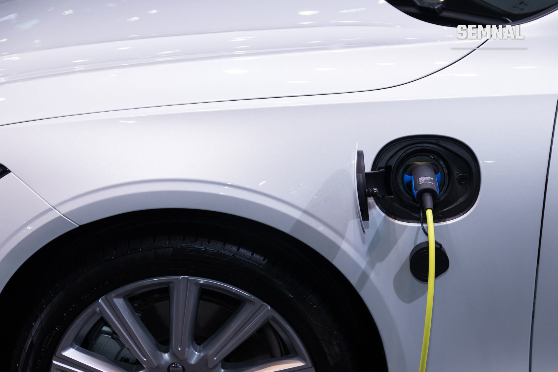 Automobil alb încărcat electric: cablu galben conectat la portul de încărcare de pe aripa din față, lângă o roată cu jantă gri (Foto: Rathaphon Nanthapreecha / Pexels)