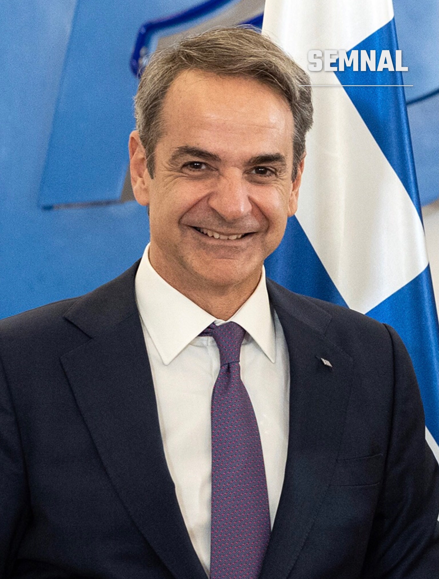Kyriakos Mitsotakis, premierul Greciei, zâmbind, în costum bleumarin și cravată mov, în fața steagului Greciei. (Foto: Yorgos Karahalis)