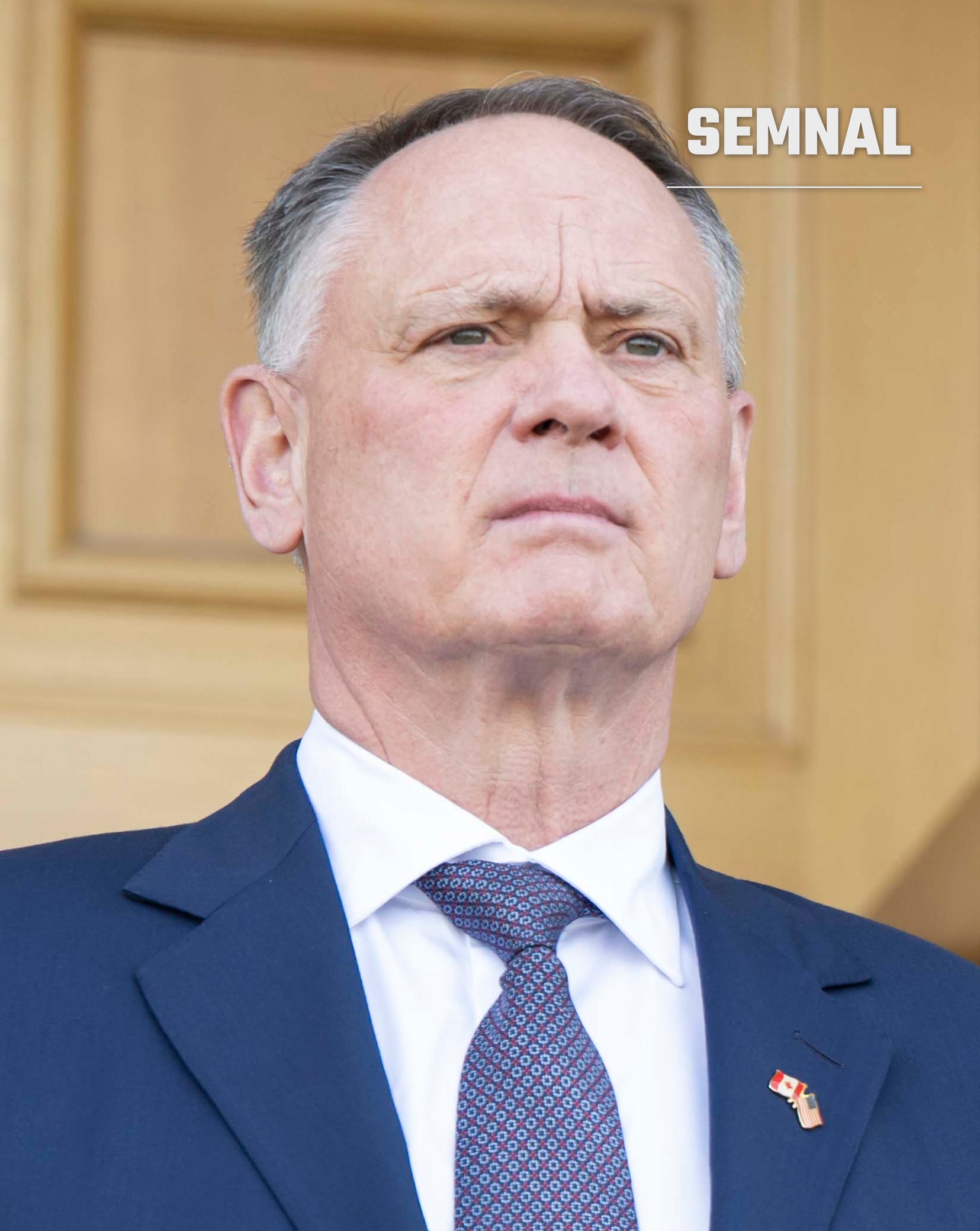 David McGuinty, ministrul apărării, în costum bleumarin și cravată cu model, pe fundal de panouri aurii. (Foto: SECWAR)