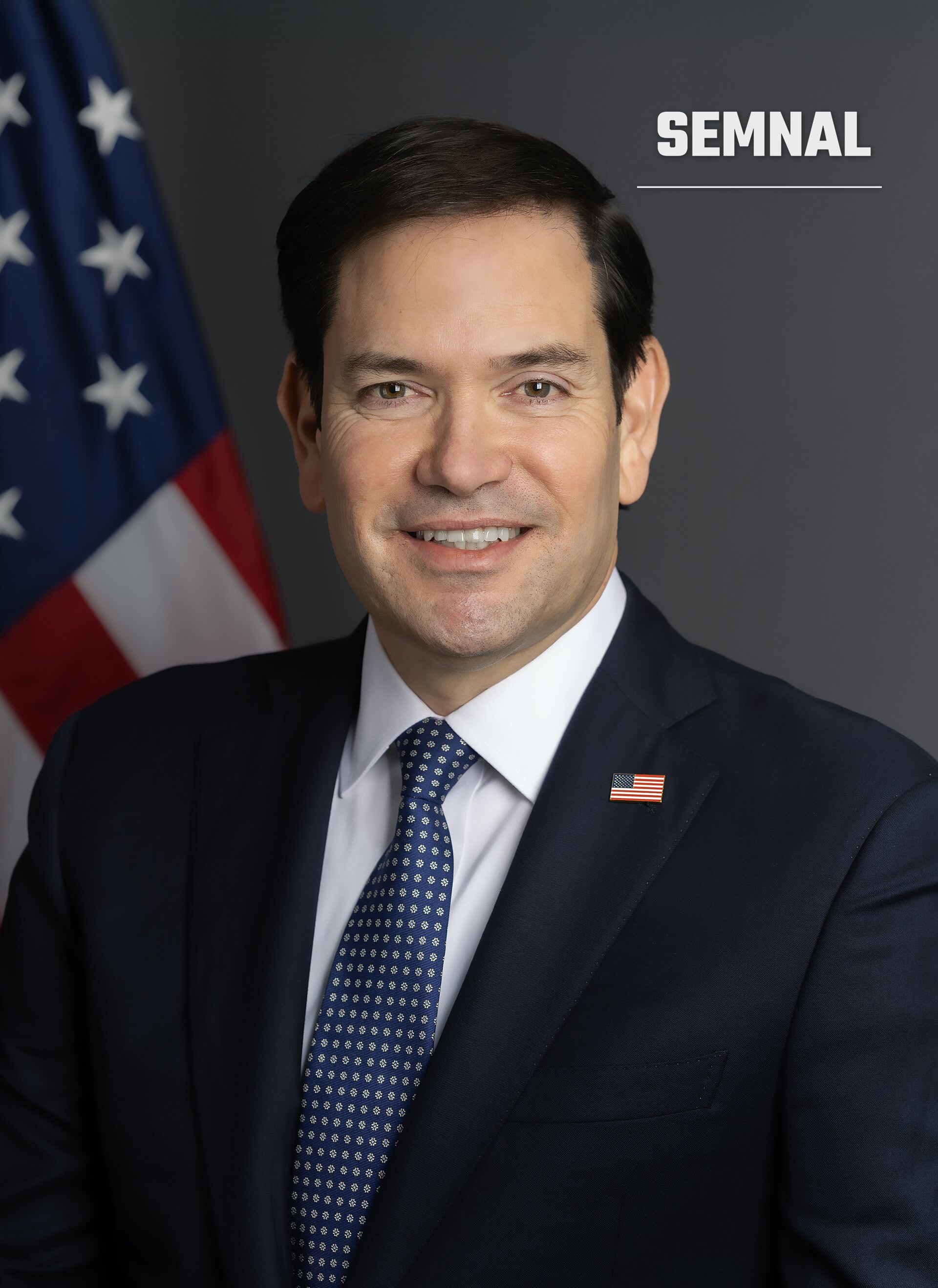 Marco Rubio, secretarul de stat al SUA, într-un portret oficial în costum bleumarin, cu drapelul american în fundal. (Foto: U.S. Department of State)