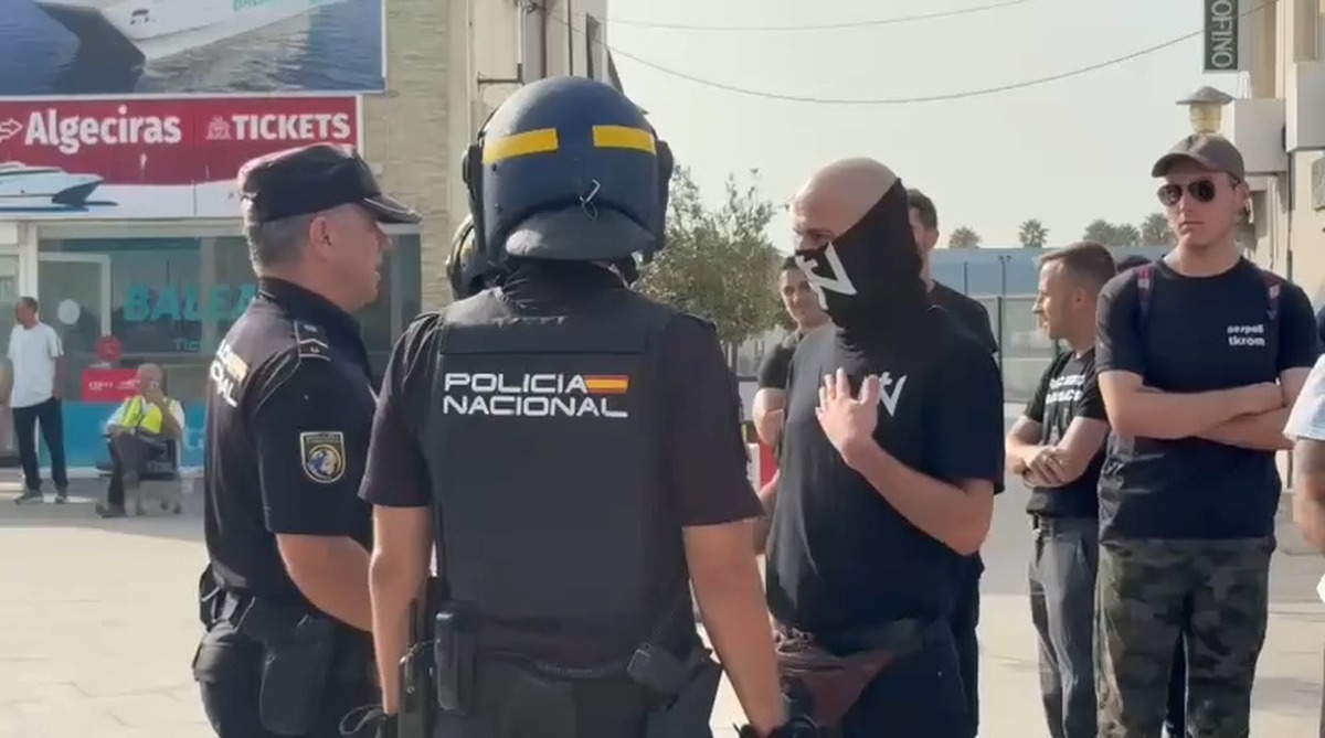Agenți ai Poliției Naționale spaniole discutând cu un grup de bărbați, unii cu fața acoperită, în portul Algeciras, punctul de îmbarcare spre Ceuta.