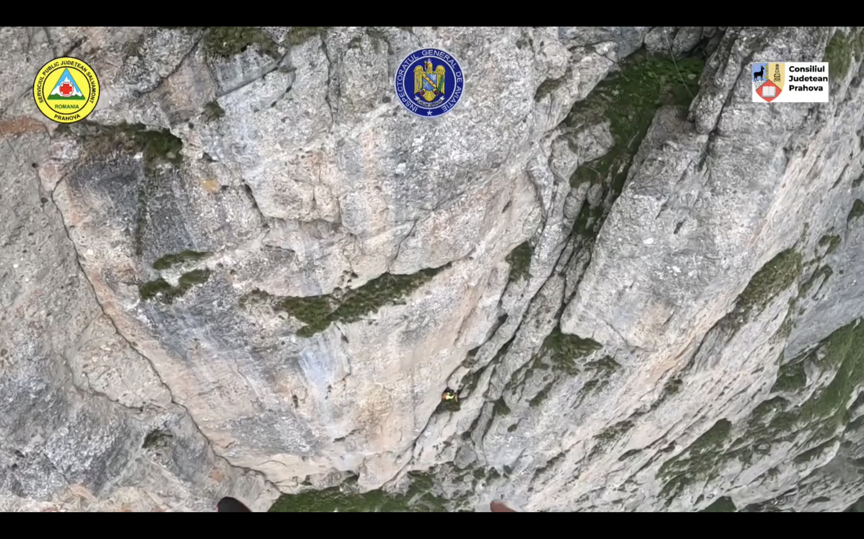 Vedere de pe casca unui salvamontist către peretele vertical al Văii Albe, cu un alpinist echipat agățat de stâncă