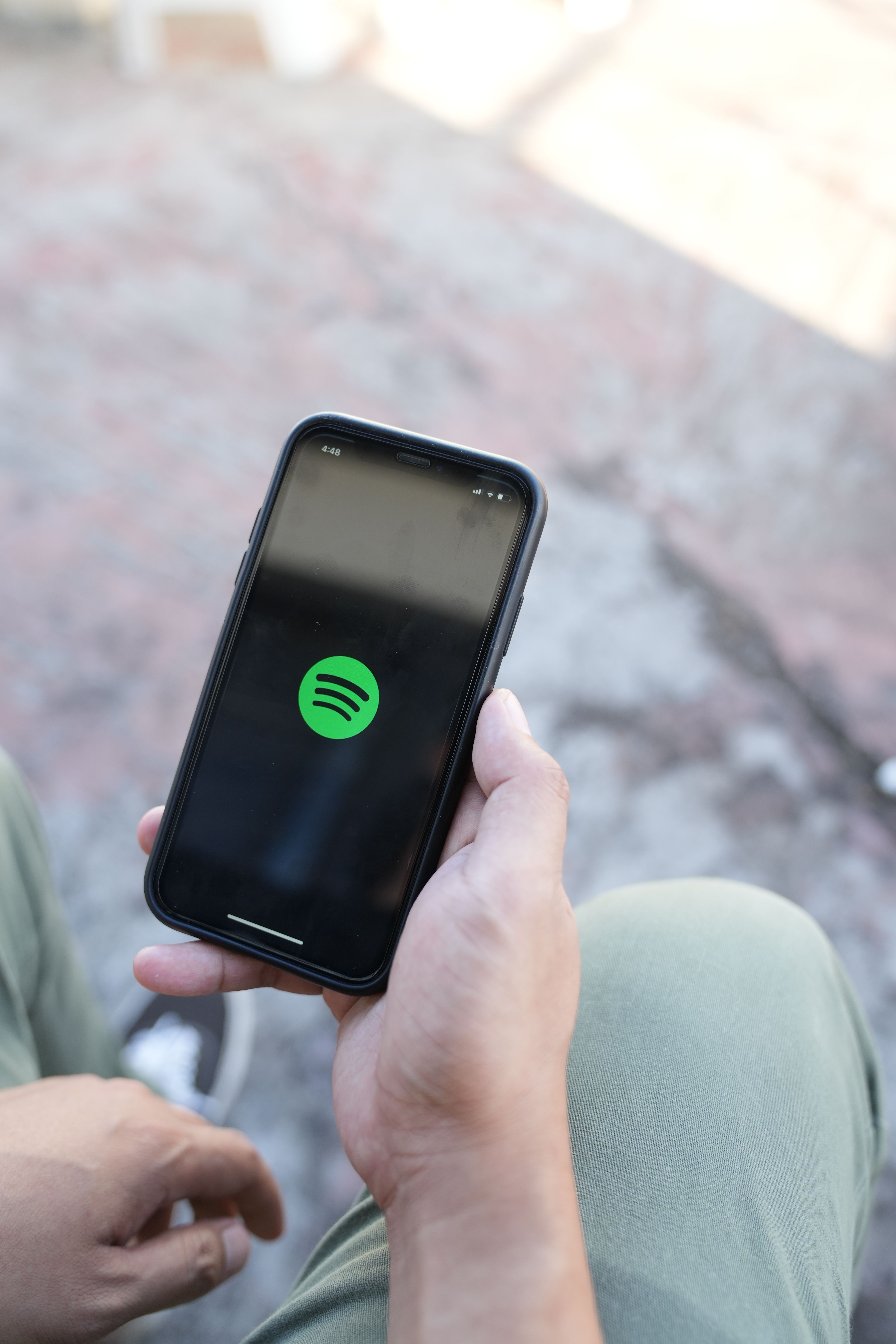 O persoană ține în mână un telefon mobil pe ecranul căruia este deschisă aplicația Spotify