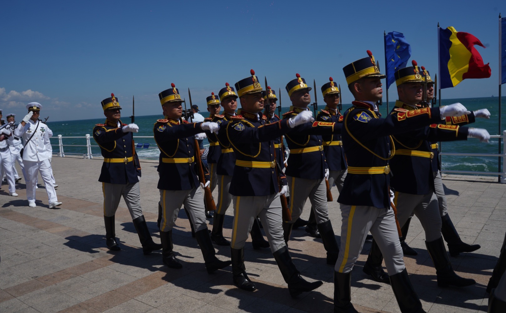 Militari din garda de onoare defilează pe faleza Constanței, cu drapelele României și Uniunii Europene în plan secund, în cadrul manifestărilor de Ziua Marinei