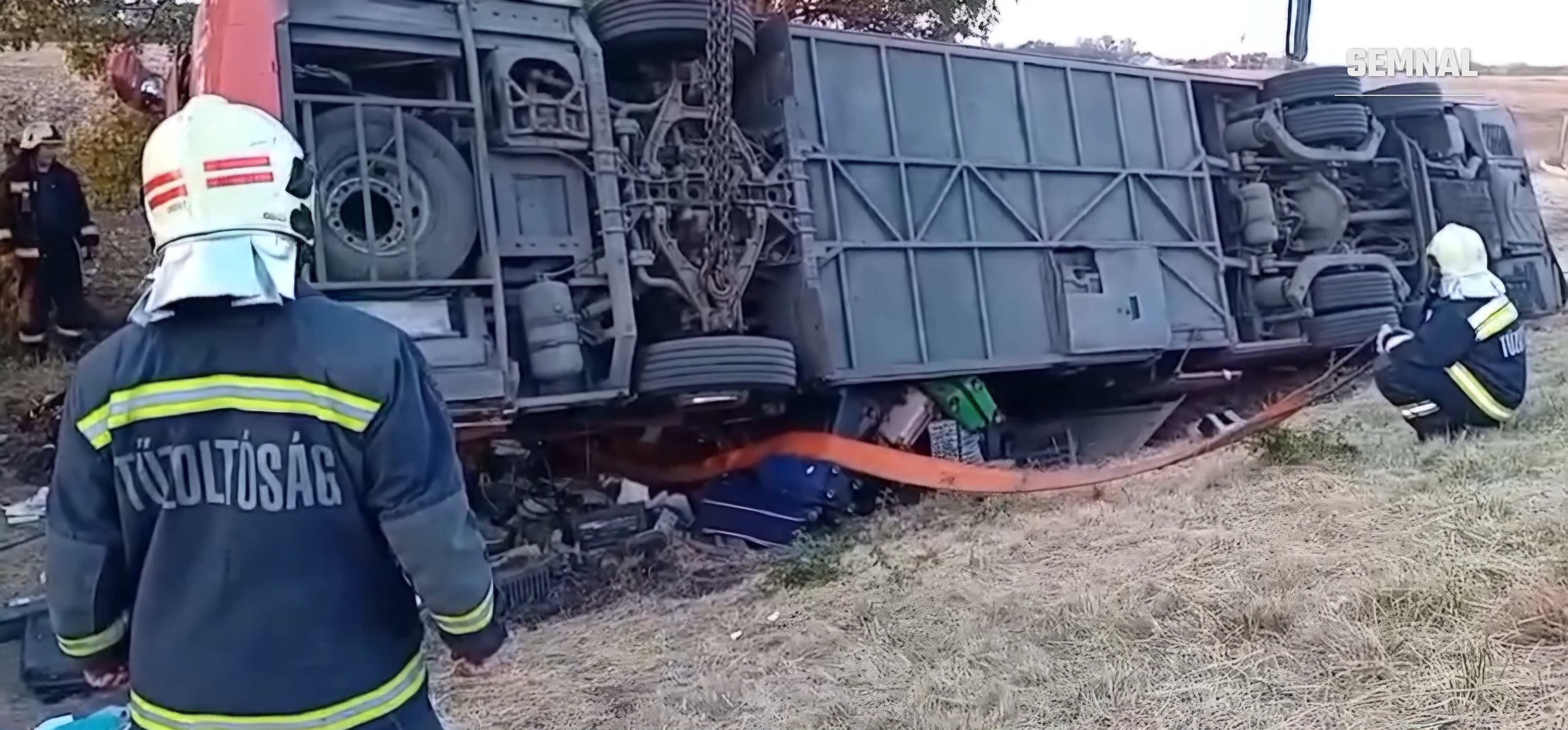 Autocarul răsturnat, văzut de aproape în lumina zilei, cu echipajele de pompieri lucrând la fața locului