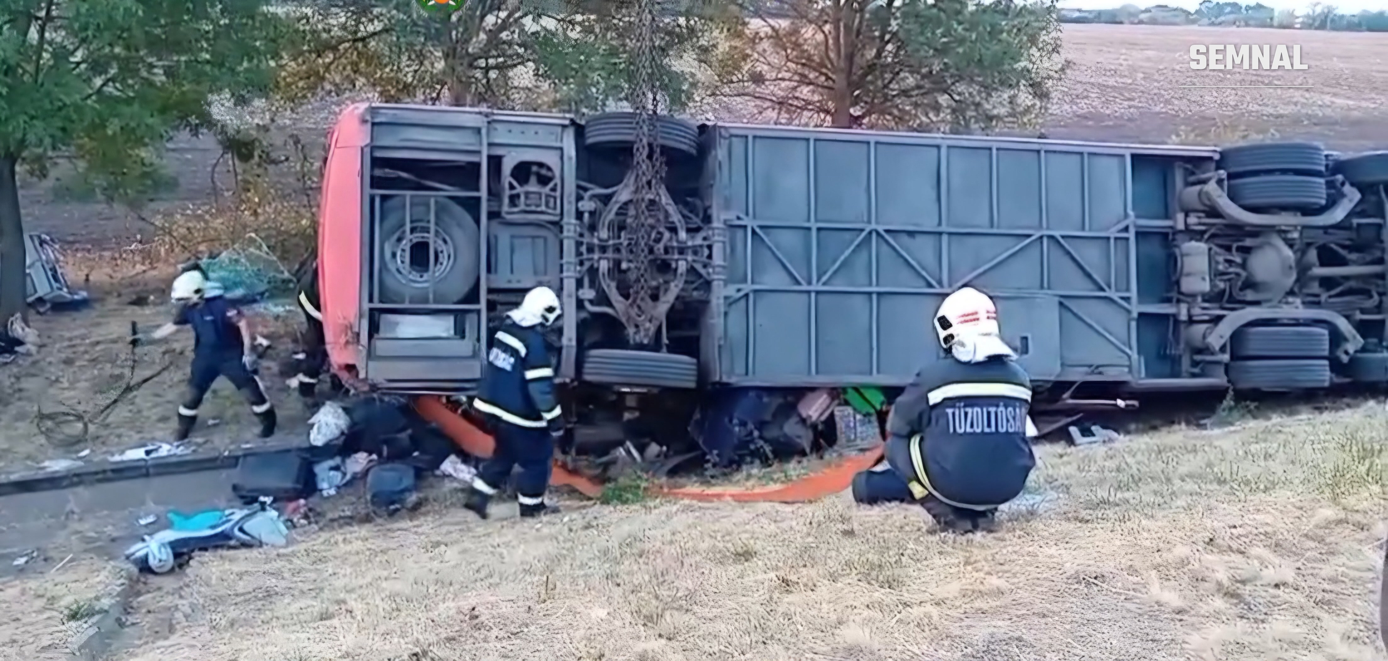 Vedere de ansamblu a autocarului răsturnat lângă copaci, cu pompierii intervenind pentru degajarea victimelor