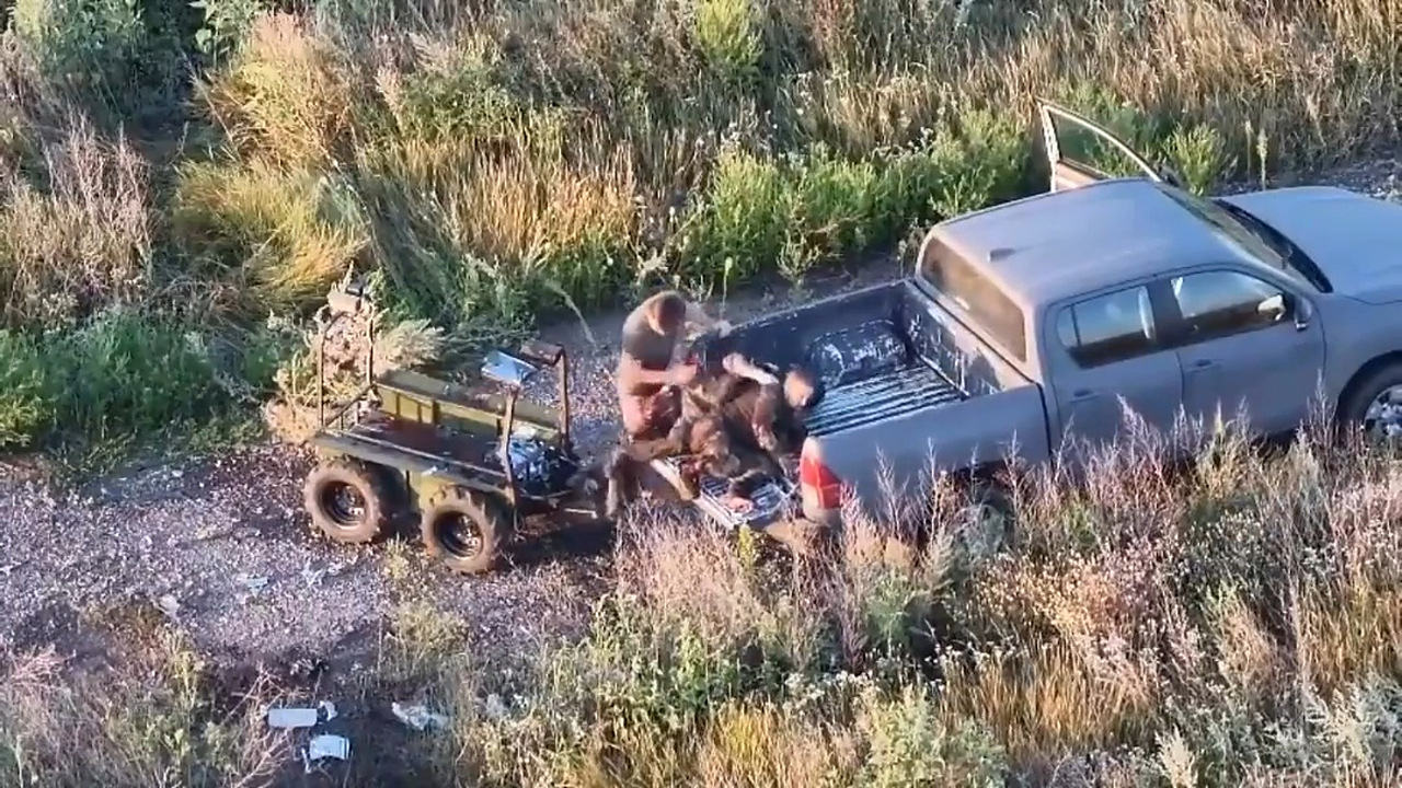 Cadru filmat din dronă: un comandant ucrainean transferă doi soldați răniți dintr-un robot terestru avariat în bena unui pickup, pe un drum de câmp