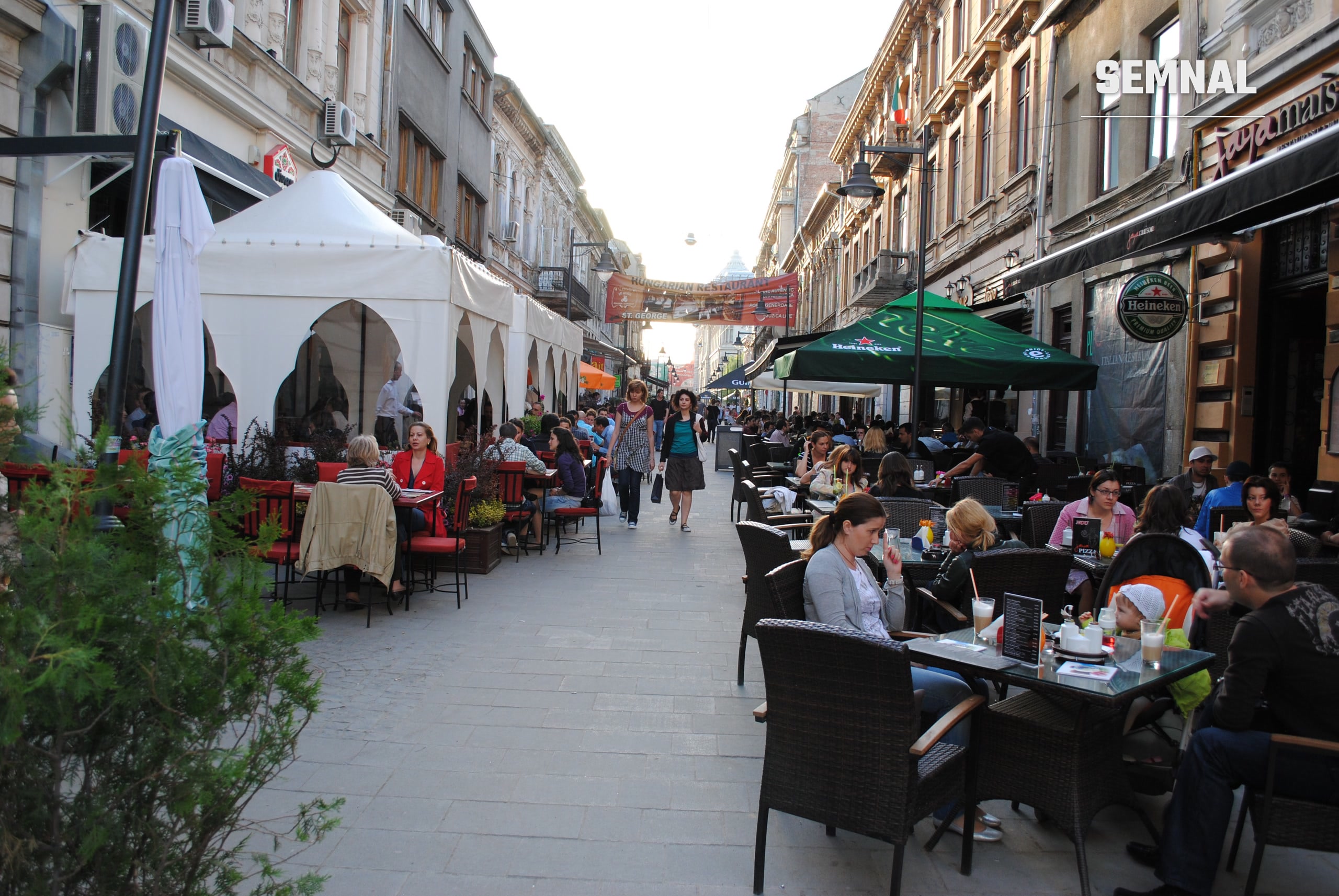 Terase cu mese pe o stradă pietonală din Centrul Vechi al Bucureștiului, cu clădiri istorice pe ambele părți