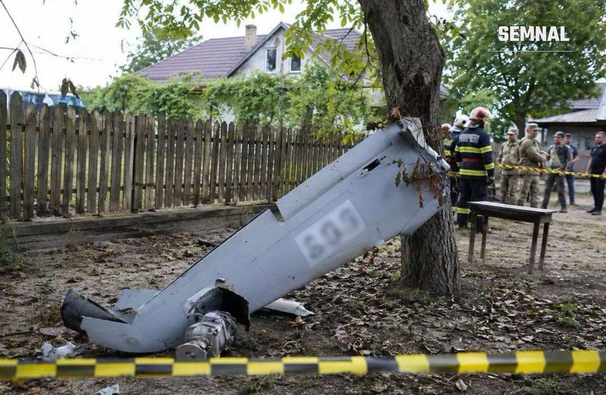 Fragment de dronă sprijinit de un copac în curtea unei case, cu pompieri și militari în spatele benzii de restricționare
