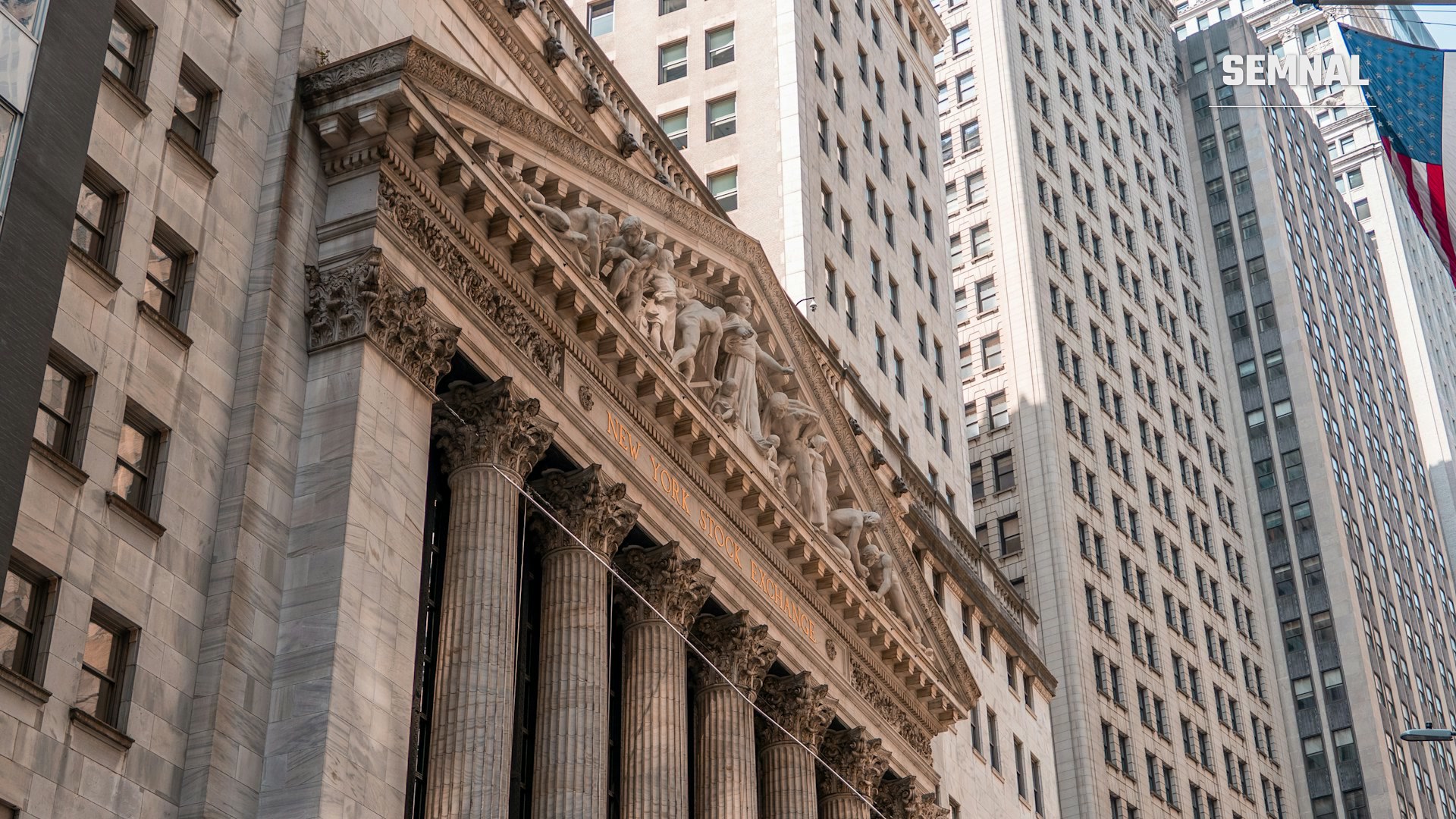 Fațada Bursei de Valori din New York (NYSE) pe Wall Street, cu coloane clasice și un steag american, într-o zi însorită.