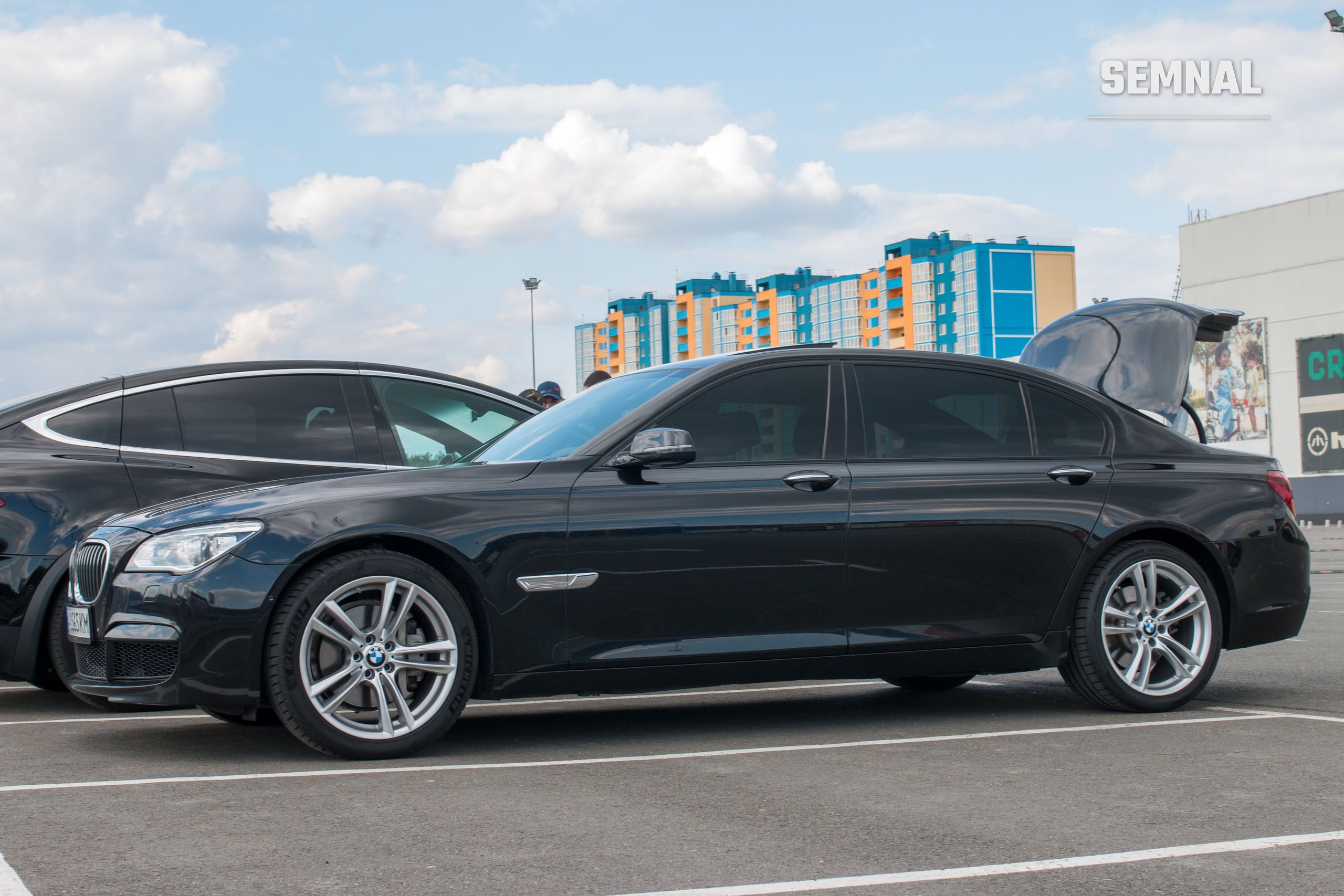BMW Seria 7, limuzină neagră, văzută din lateral, parcată într-un cadru urban modern