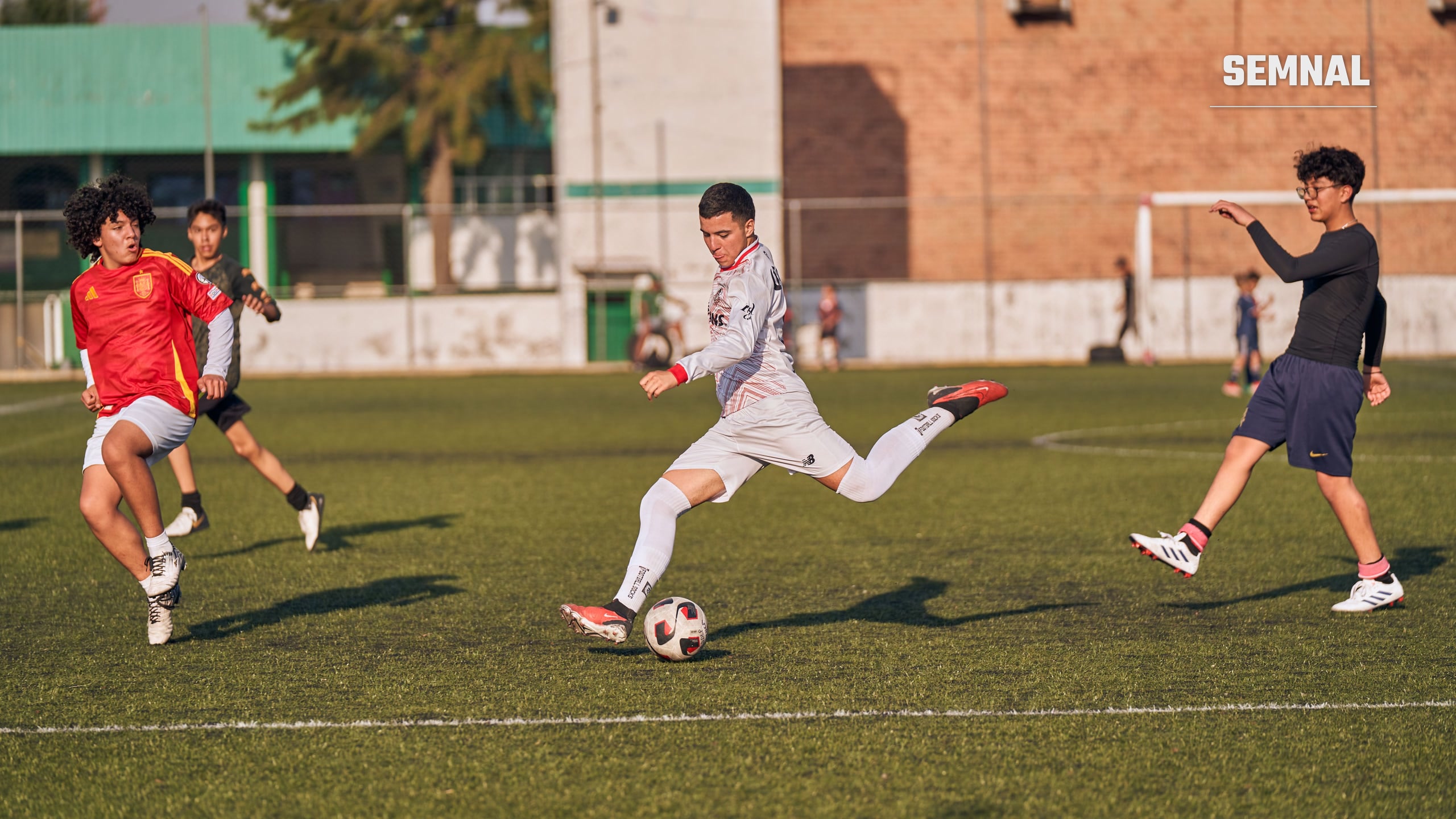 Grup de adolescenți aleargă pe un teren de fotbal în timpul unui meci, într-o zi însorită