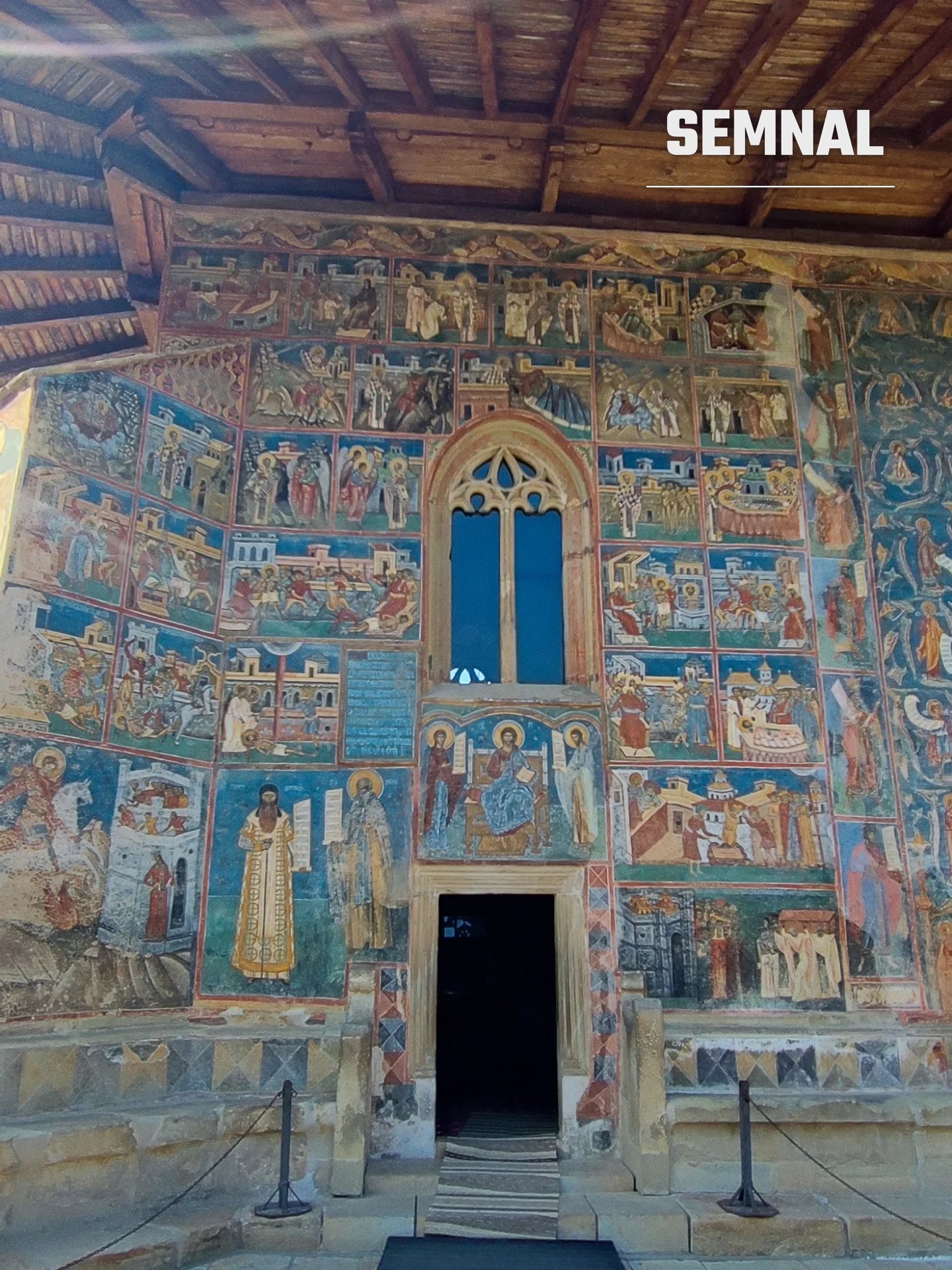 Fațada exterioară pictată, cu fereastra în stil gotic și intrarea în biserică