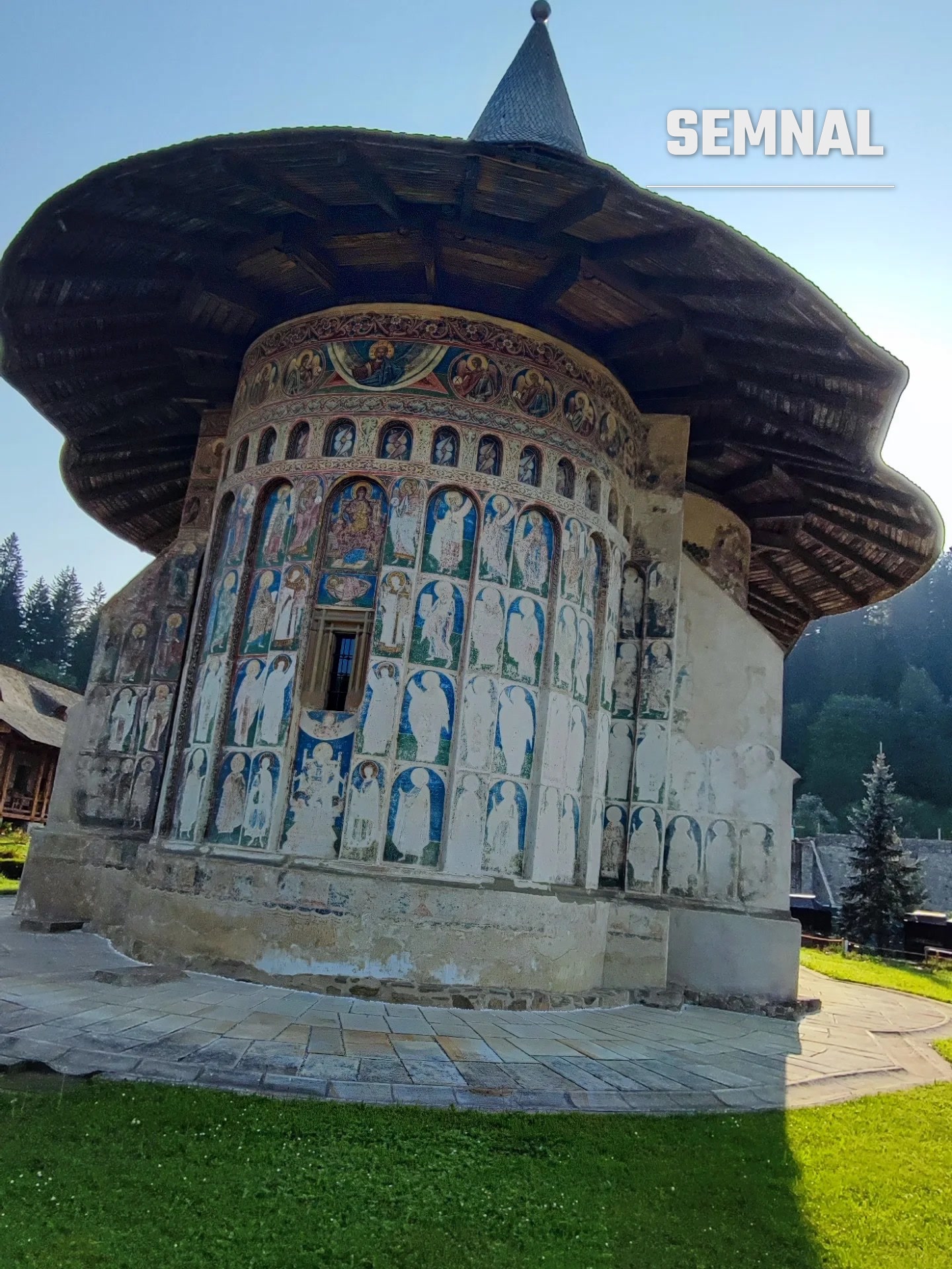 Absida pictată, cu șiruri de sfinți sub streașina largă din șindrilă