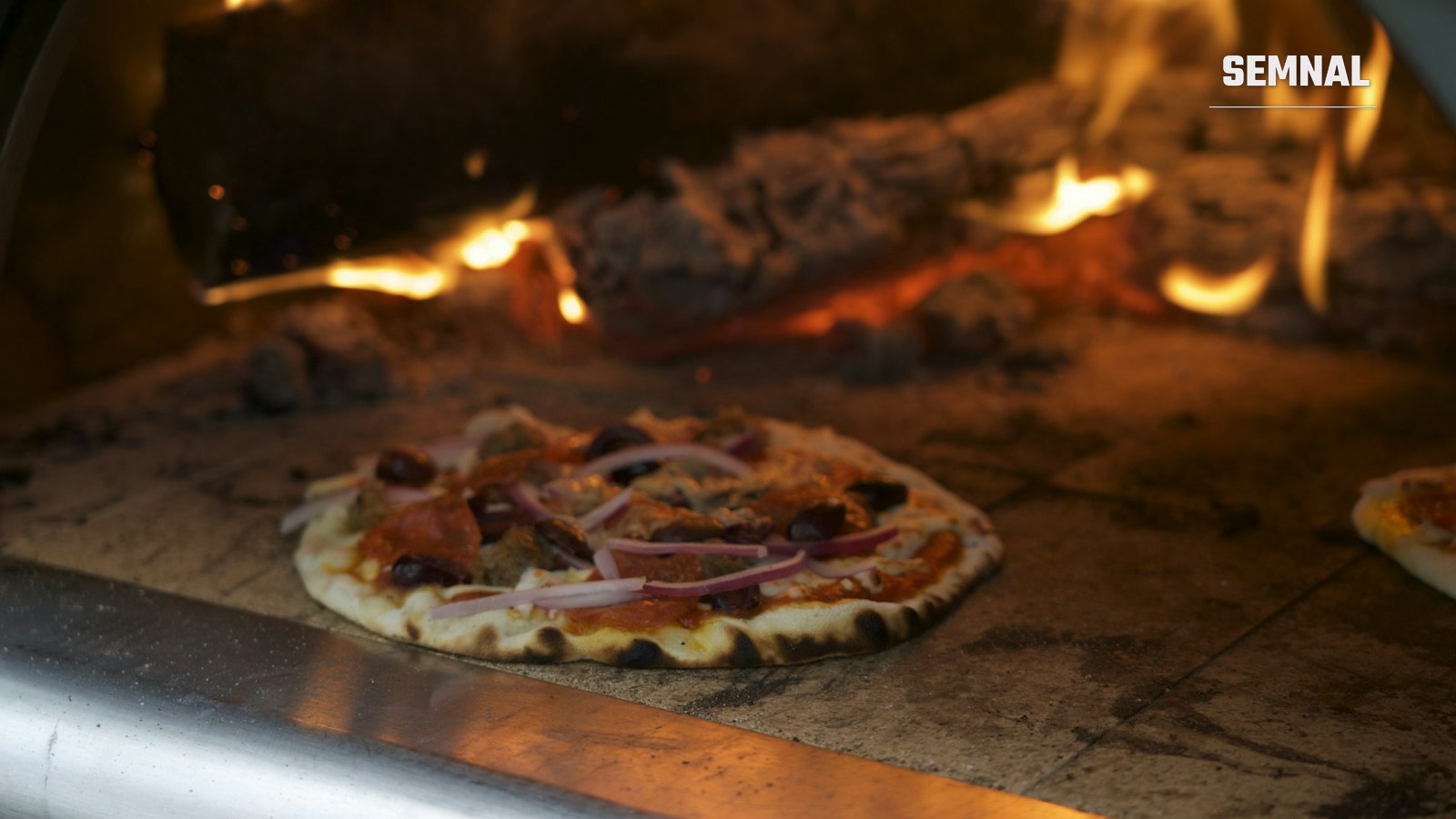 Pizza napoletană gătită într-un cuptor cu lemne, cu flăcările vizibile în fundal