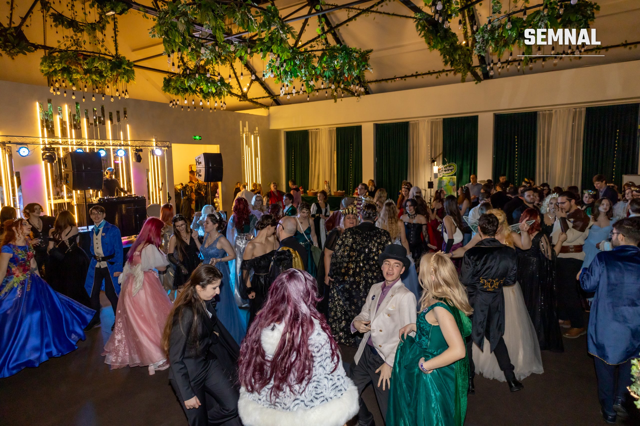 Sala balului fantasy, decorată cu verdeață și lumini, plină de invitați costumați
