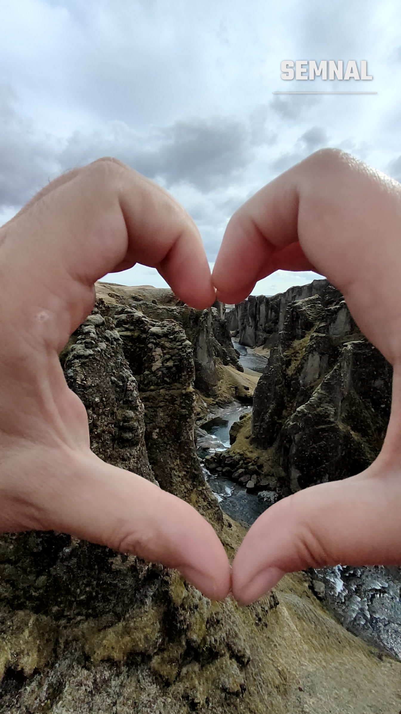 Mâini formând o inimă, cu canionul Fjaðrárgljúfur din Islanda în cadru