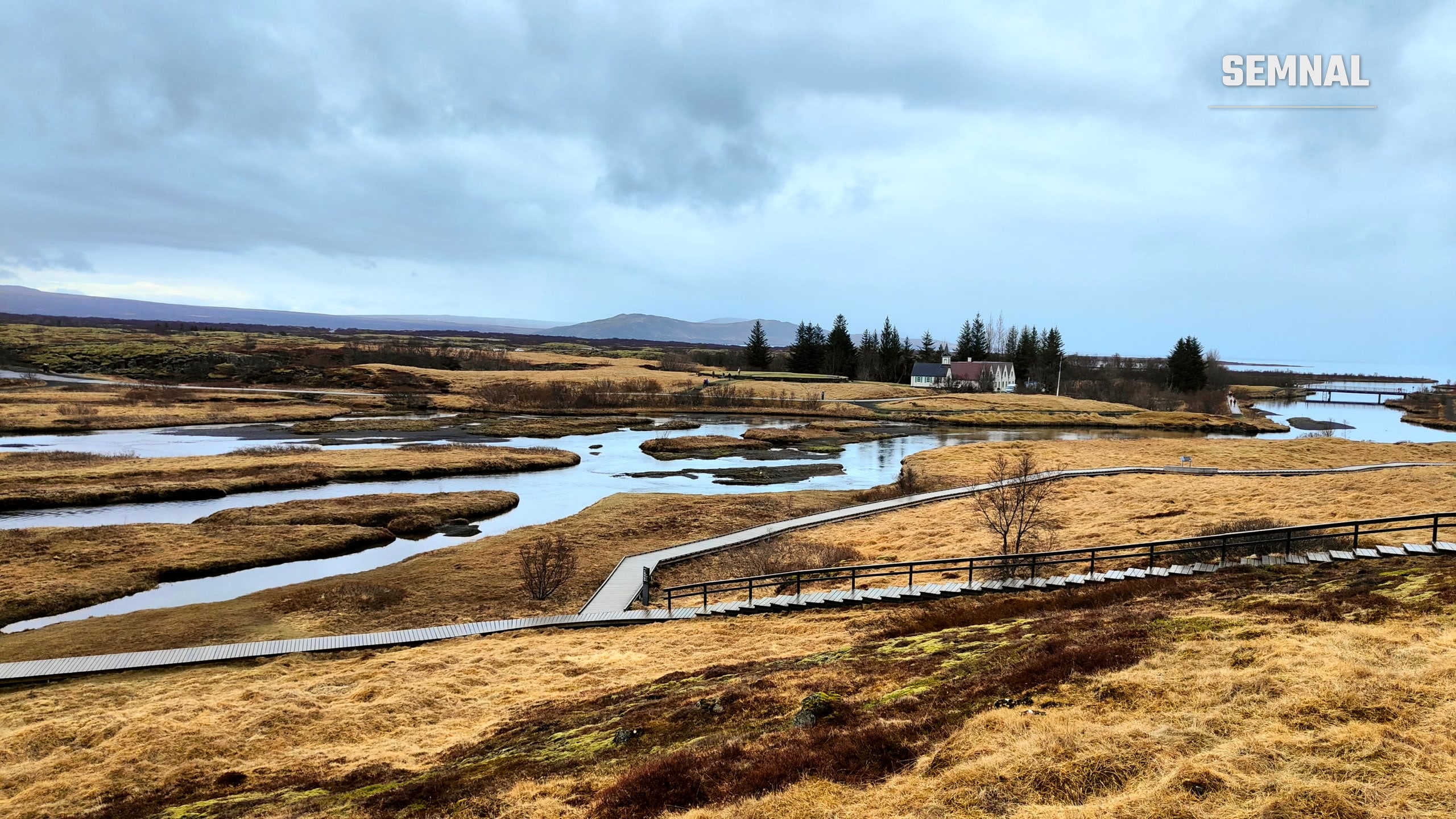 Zona umedă a Parcului Național Þingvellir, cu pasarele de lemn peste apă și munți în fundal