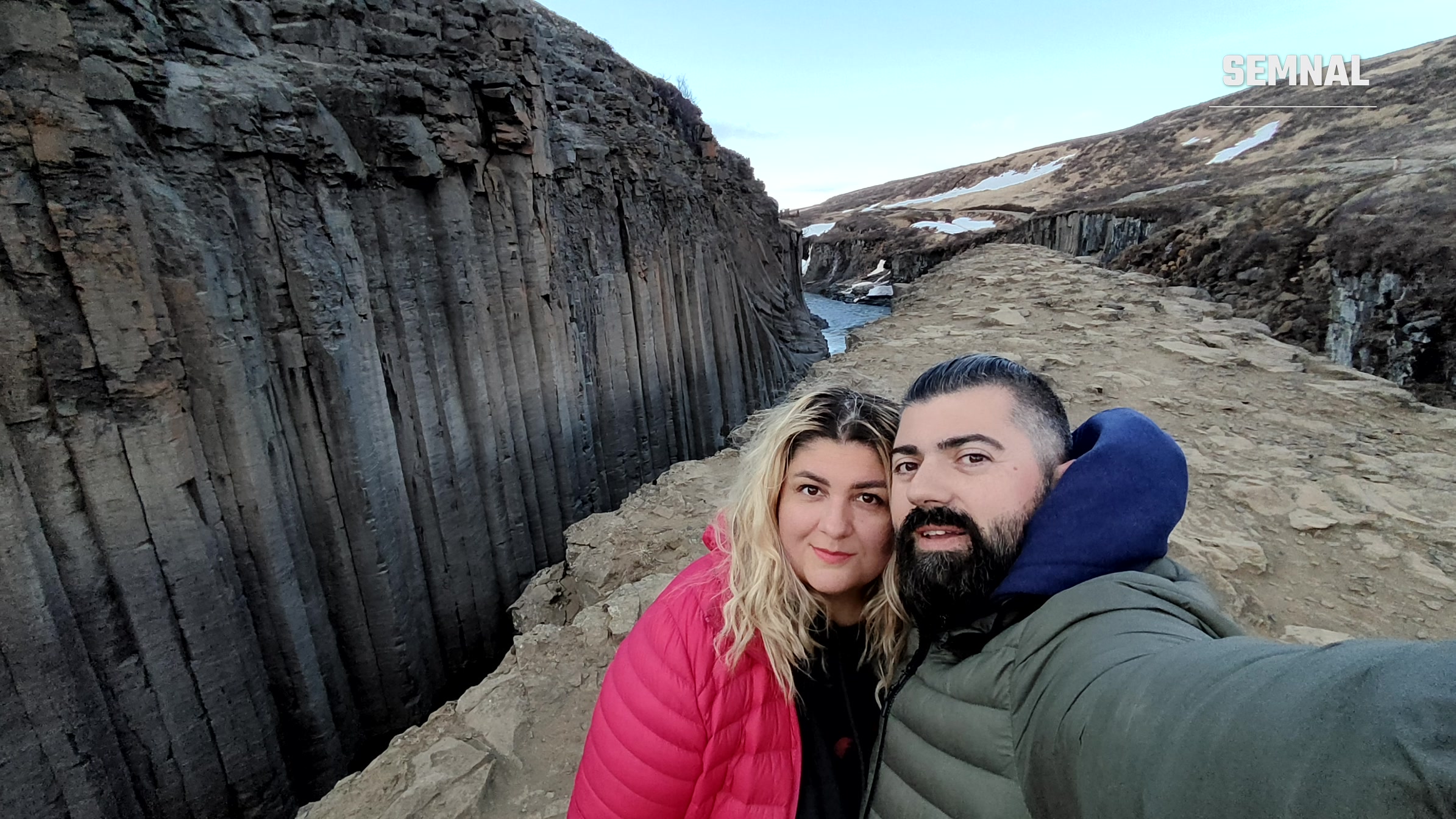 Mugur și Alina Petrea la marginea canionului Stuðlagil, cu coloane de bazalt și un râu turcoaz în spate