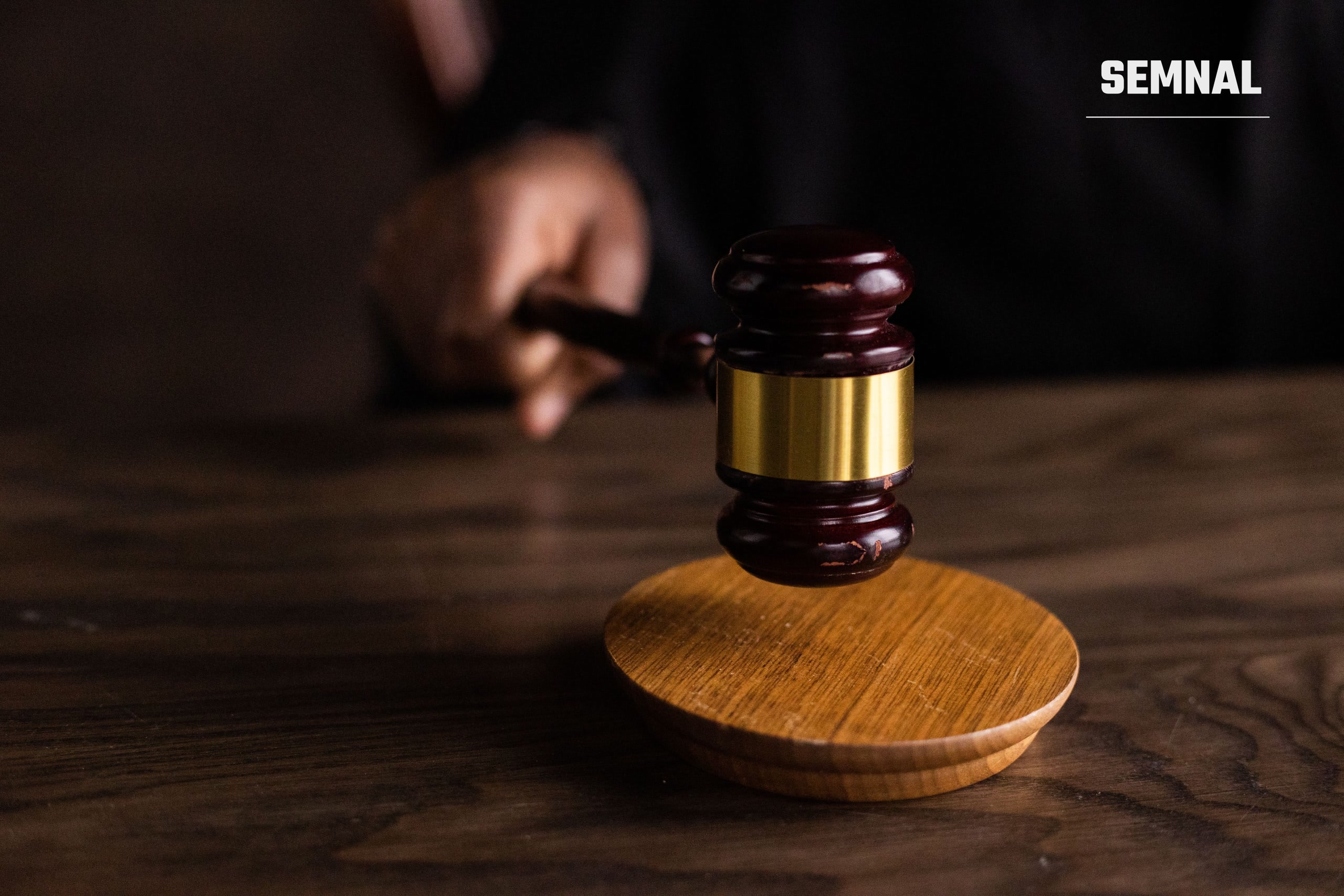 Mână care ține un ciocănel de judecător din lemn deasupra suportului rotund, pe o masă de lemn