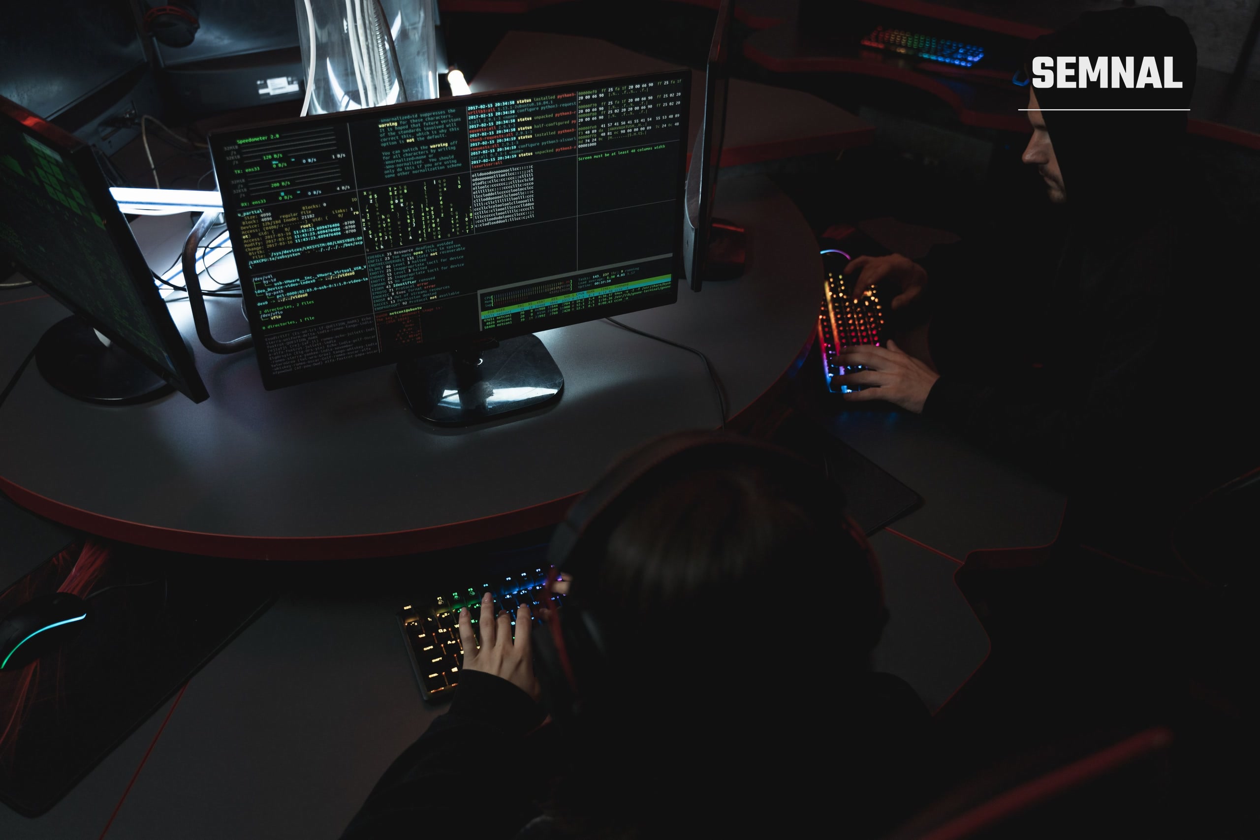Două persoane lucrează la calculatoare într-o cameră slab luminată, simbol pentru fraudele online