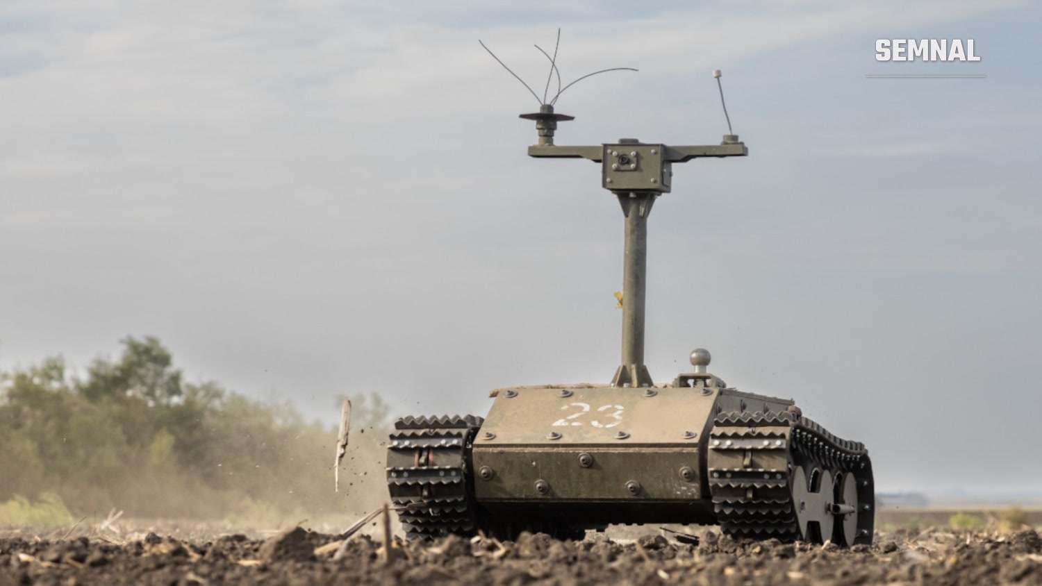 Robot terestru ucrainean pe șenile, cu catarg de antene și număr alb vopsit pe cocă, înaintează pe un câmp arat, sub un cer înnorat.