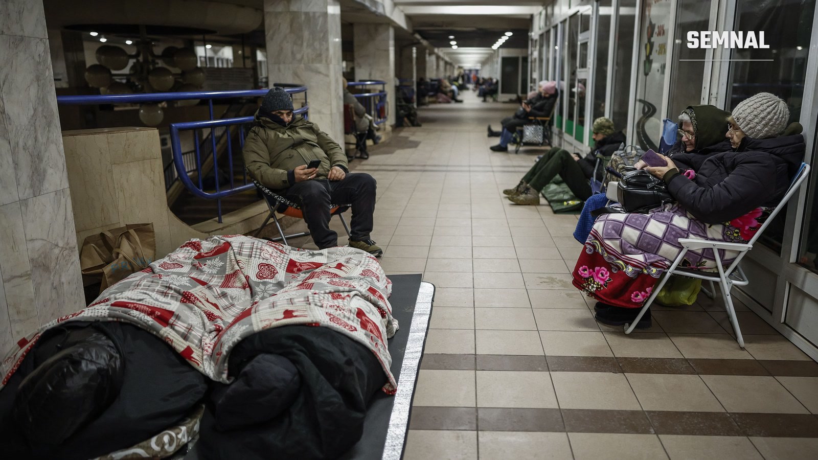 Oameni adăpostiți pe peronul unei stații de metrou din Kiev în timpul unei alerte aeriene: unii dorm pe saltele, alții stau pe scaune pliante