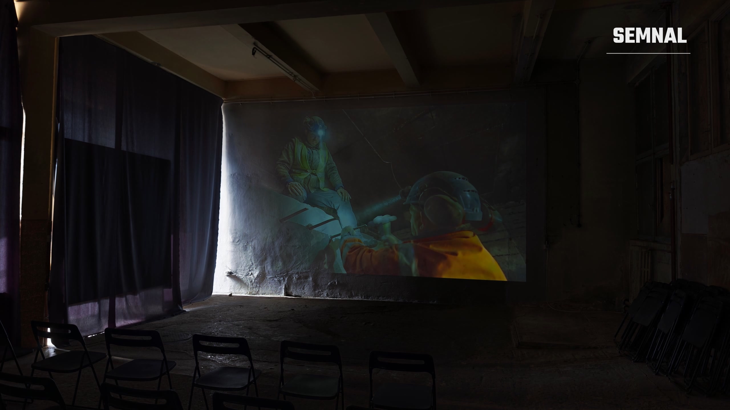 Film proiectat pe un perete nefinisat, cu muncitori într-o galerie subterană. Fotografie realizată de Lucian Dinu