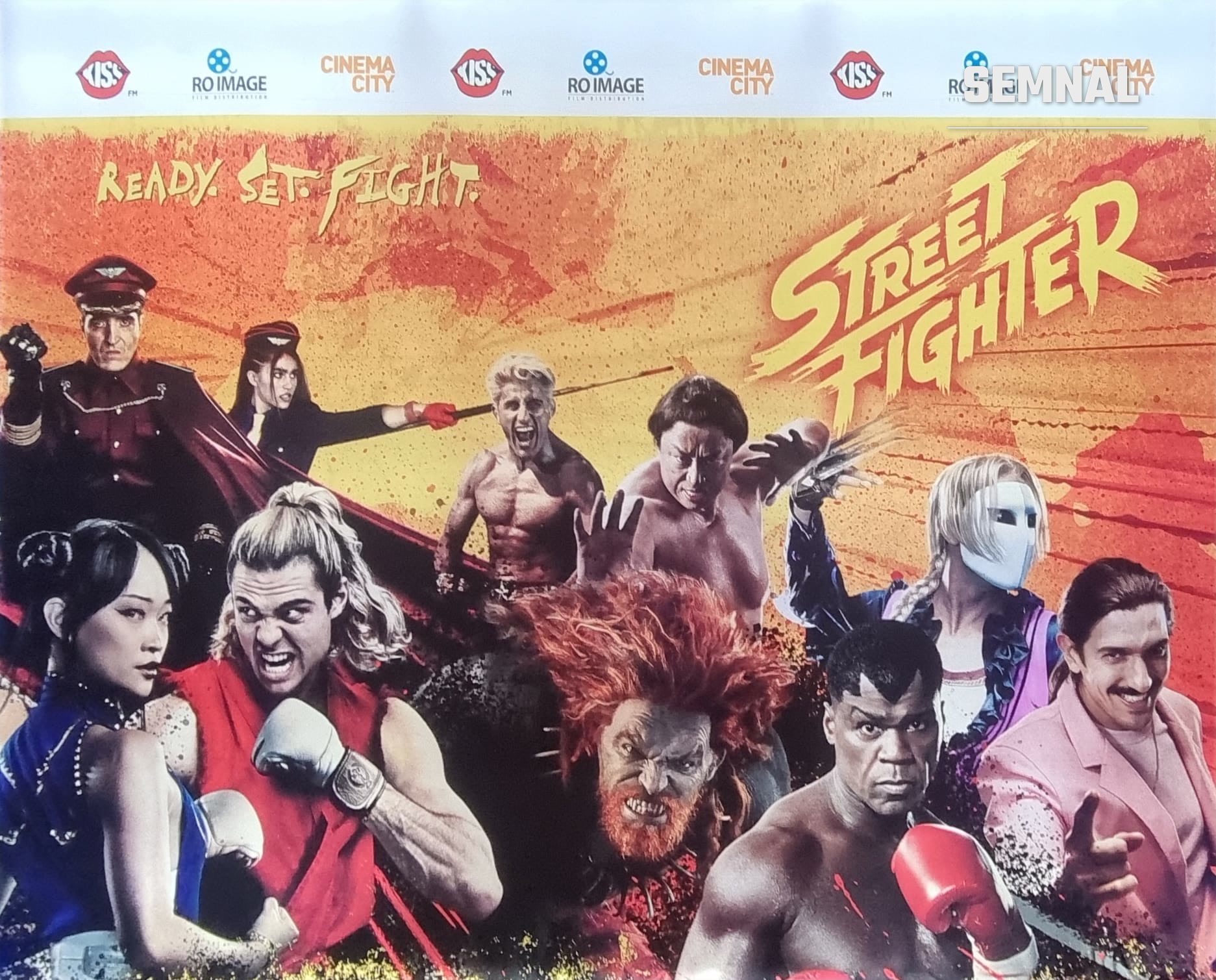 Panoul filmului Street Fighter de la avanpremiera de la Cinema City Mega Mall, cu personajele filmului pe fundal portocaliu și sigla Street Fighter