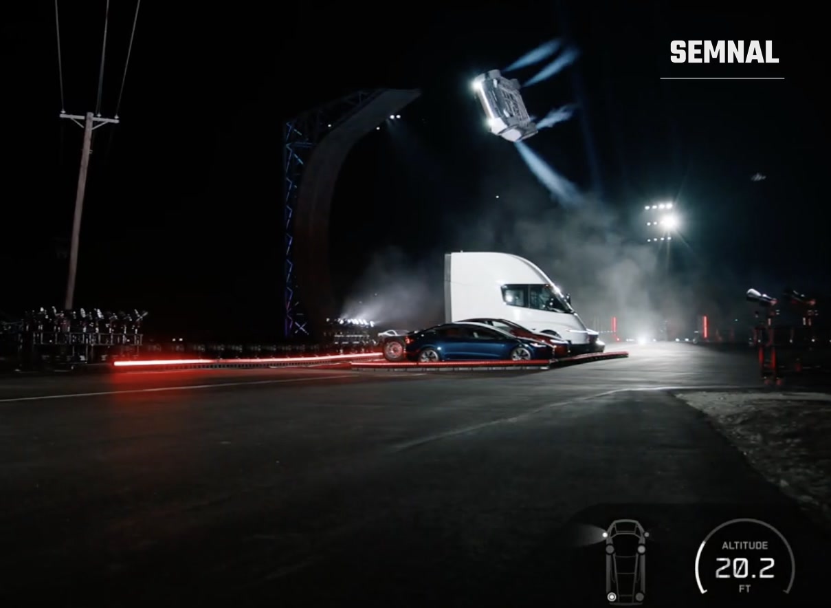 Noul Tesla Roadster, cu roțile în sus, deasupra unui camion Tesla Semi și a două mașini, noaptea, la baza SpaceX din McGregor, Texas