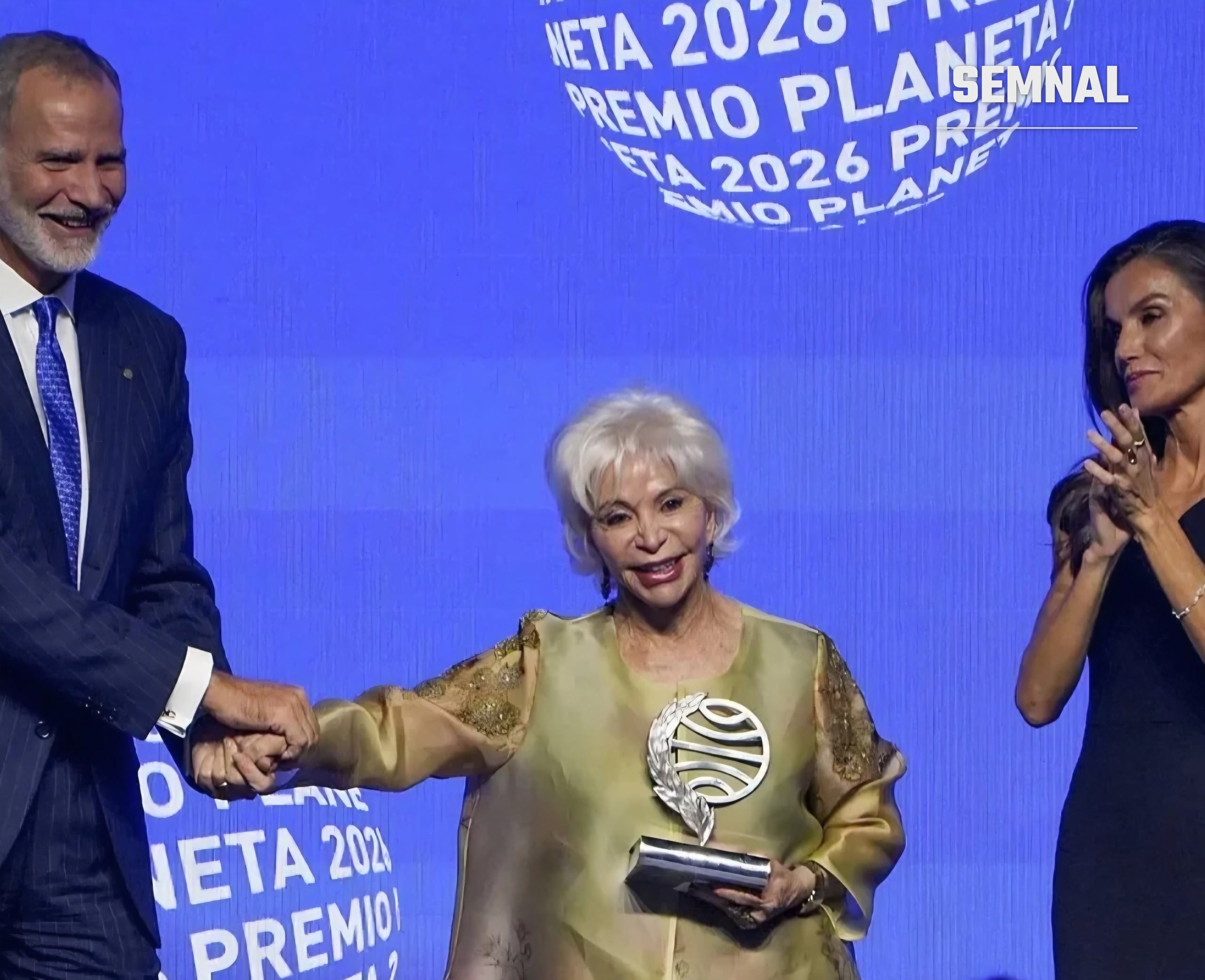 Isabel Allende cu trofeul Premiului Planeta 2026, ținută de mână de regele Felipe al VI-lea, lângă regina Letizia care aplaudă, pe scena galei