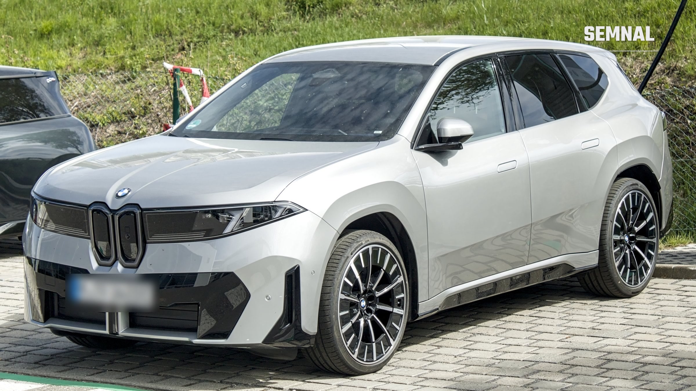 SUV-ul electric BMW iX3 din generația Neue Klasse, în culoare gri deschis, parcat pe o alee pavată, văzut din față și din lateral