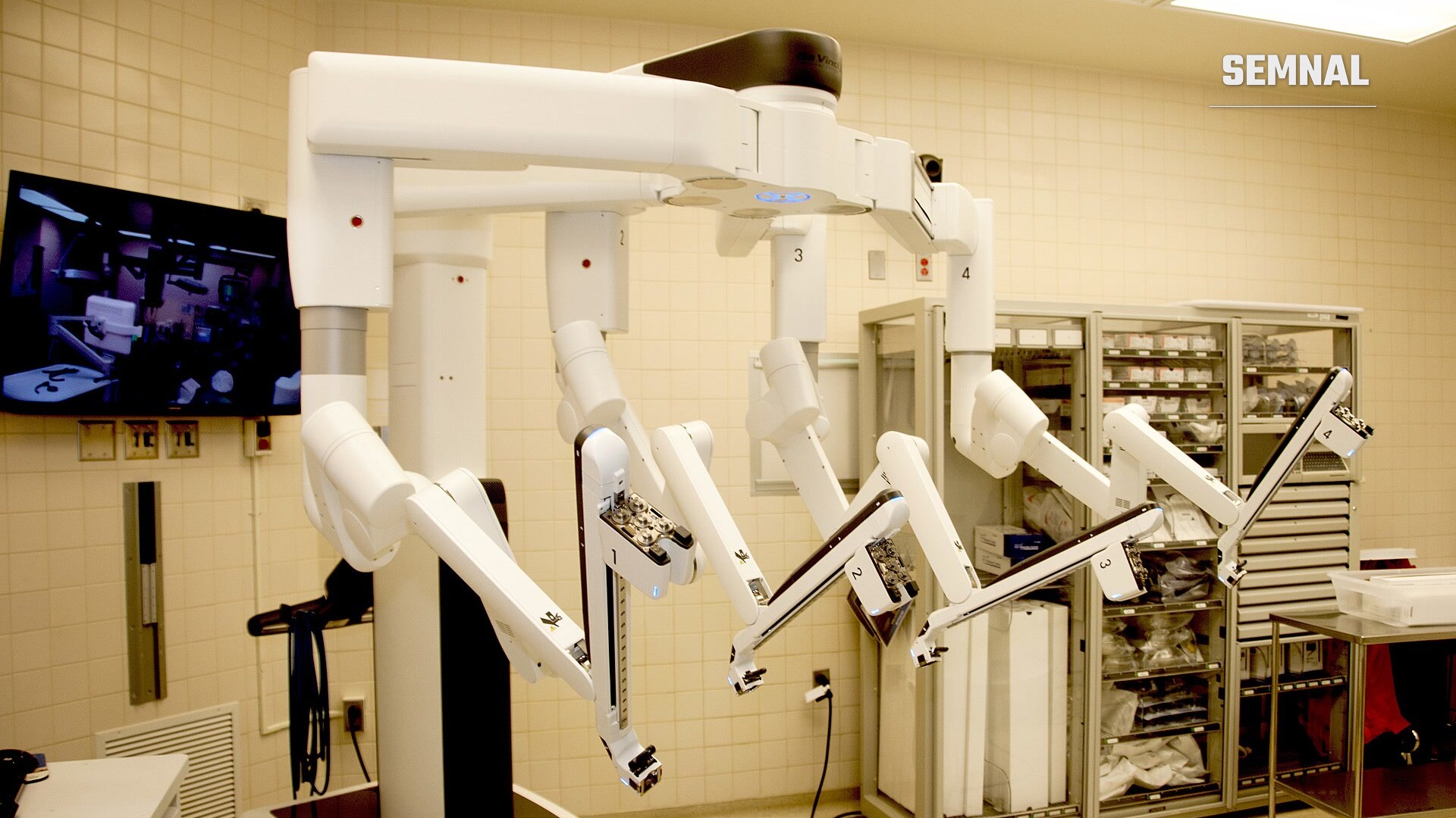 Robot chirurgical Da Vinci Xi cu patru brațe articulate albe, într-o sală de operație, lângă un monitor și un dulap cu instrumente