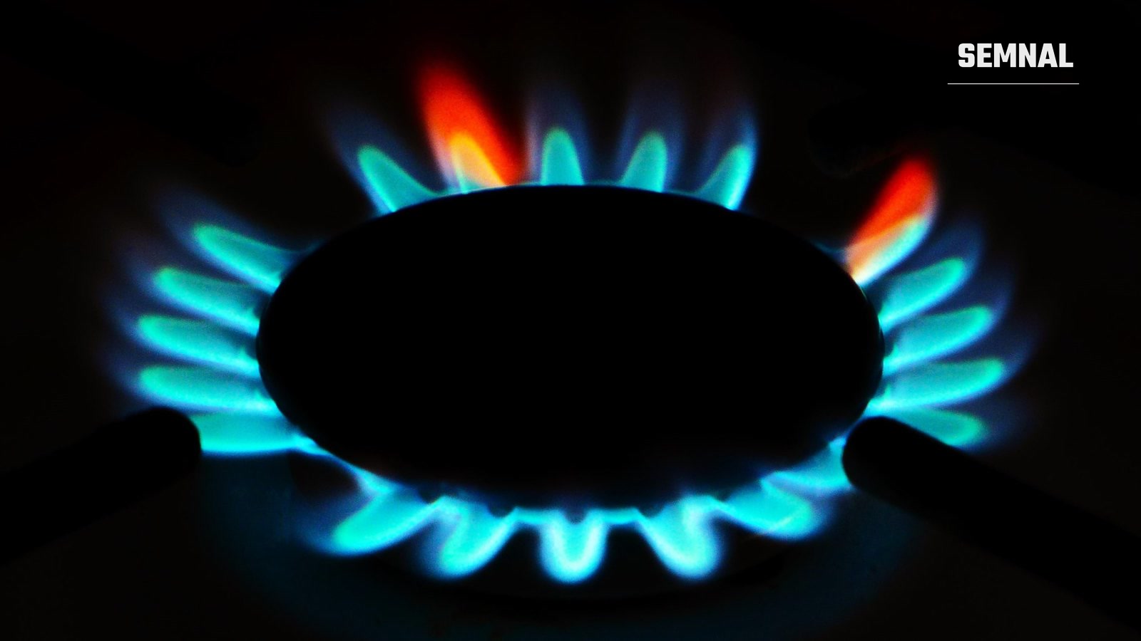 Flacără albastră la arzătorul unui aragaz pe gaz, fotografiată pe fundal întunecat